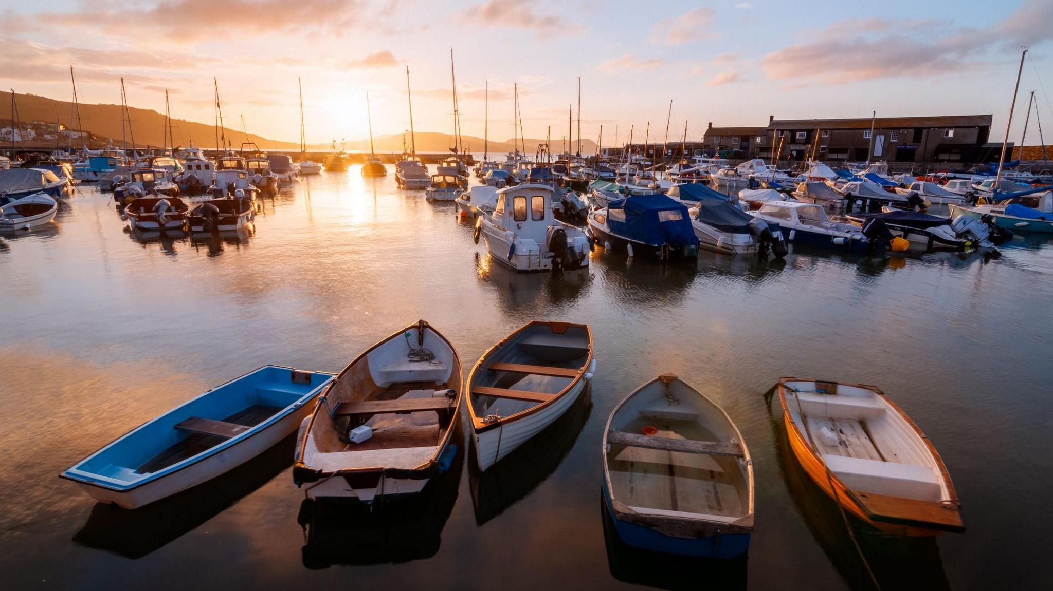 A general view of Lyme Regis harbour in June, with the sun setting in the background 