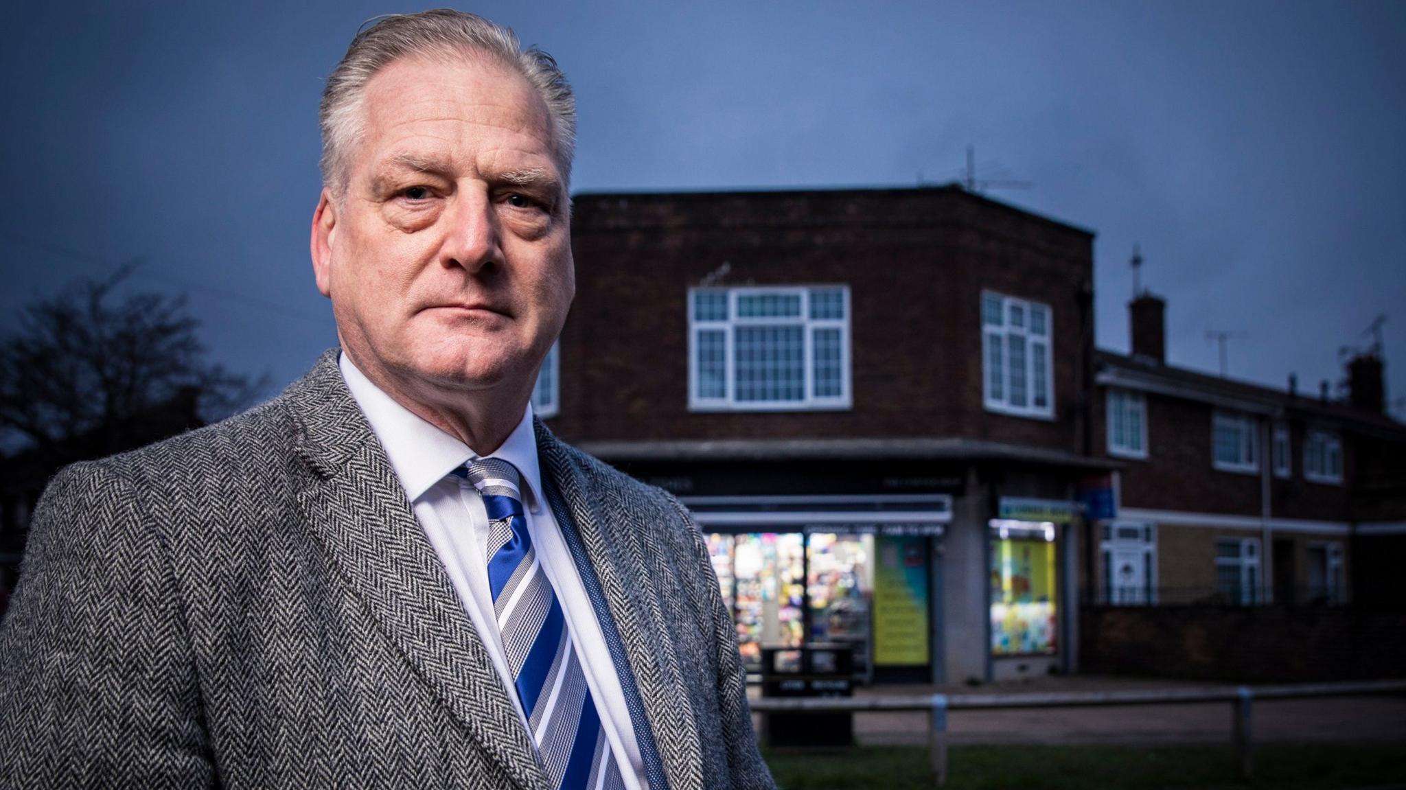 Carl Foster wearing a grey suit and stood in front of the shop where Carol Morgan was killed