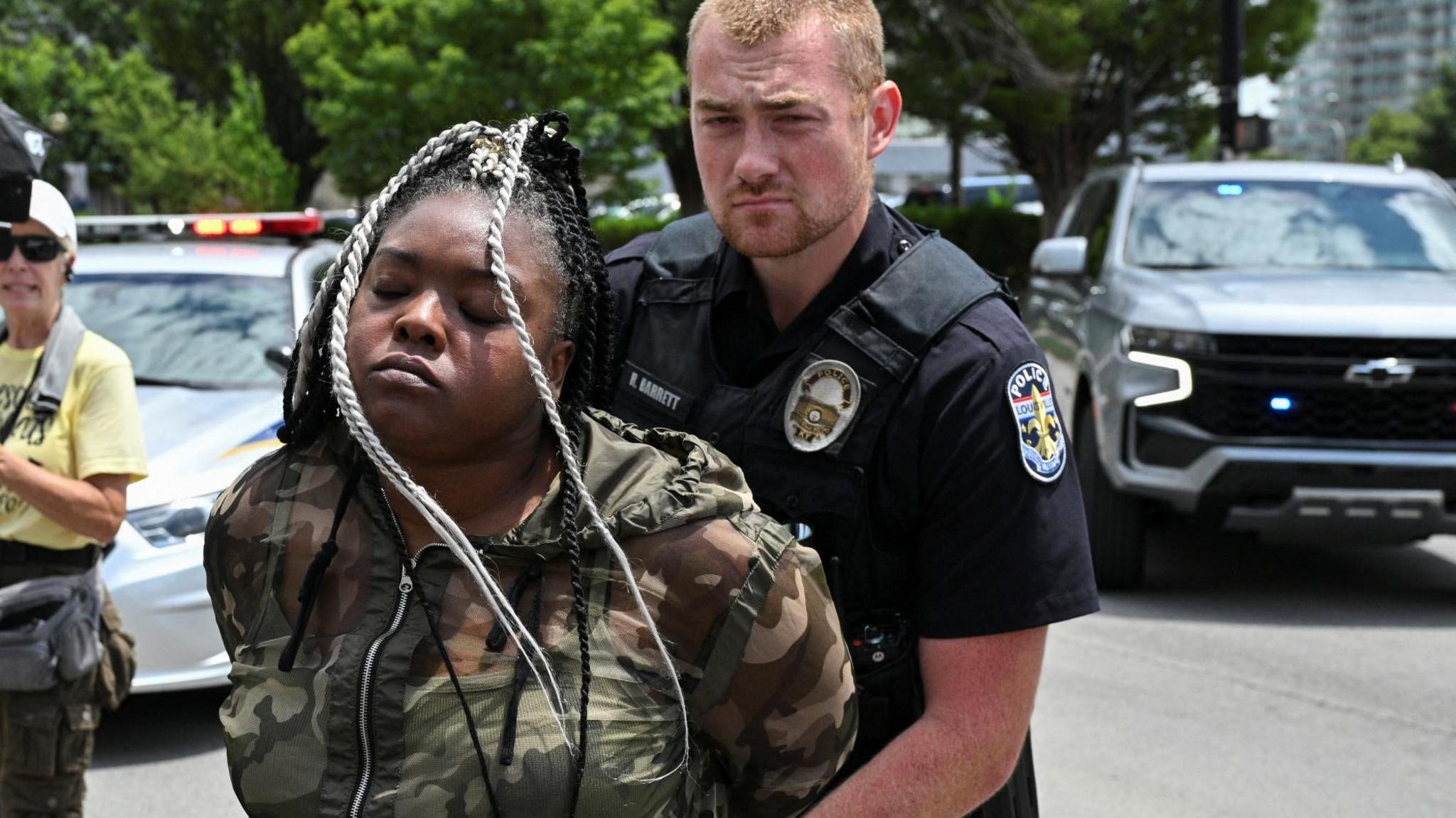 A police officer holds a woman's hands behind her back as he arrests her on the street