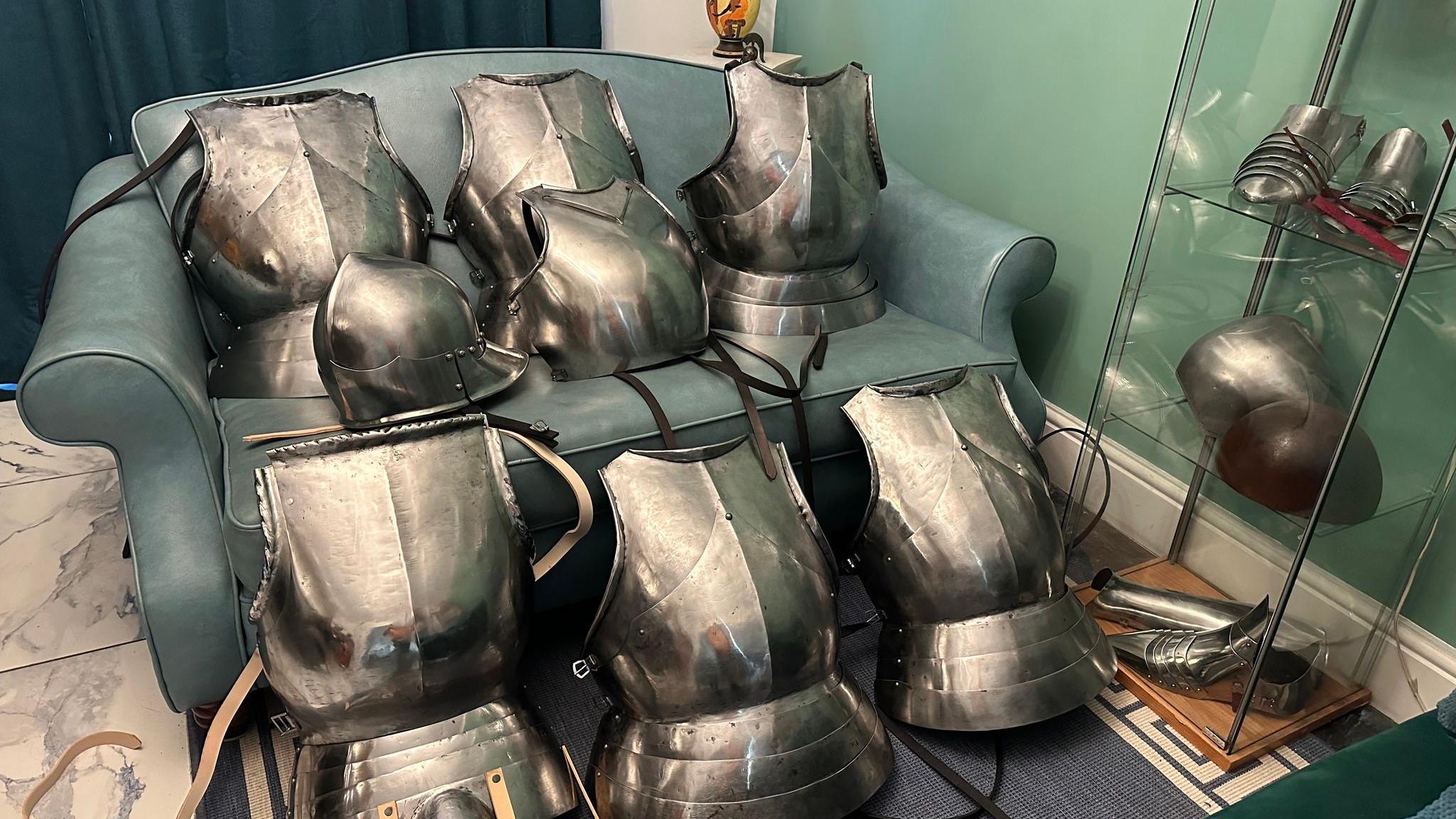 Seven breastplates and a helmet stacked on a sofa in a domestic living room