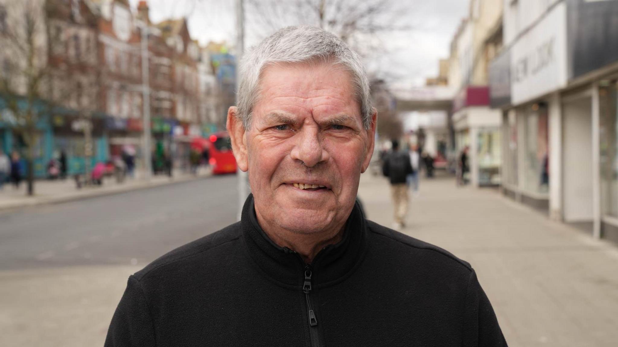 Malcom Taylor wearing a black jumper standing in Clacton town centre. He is smiling into the camera. 