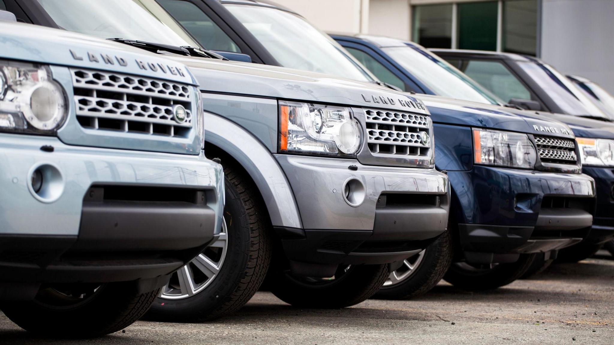Landrovers sit in a row in a car dealership.