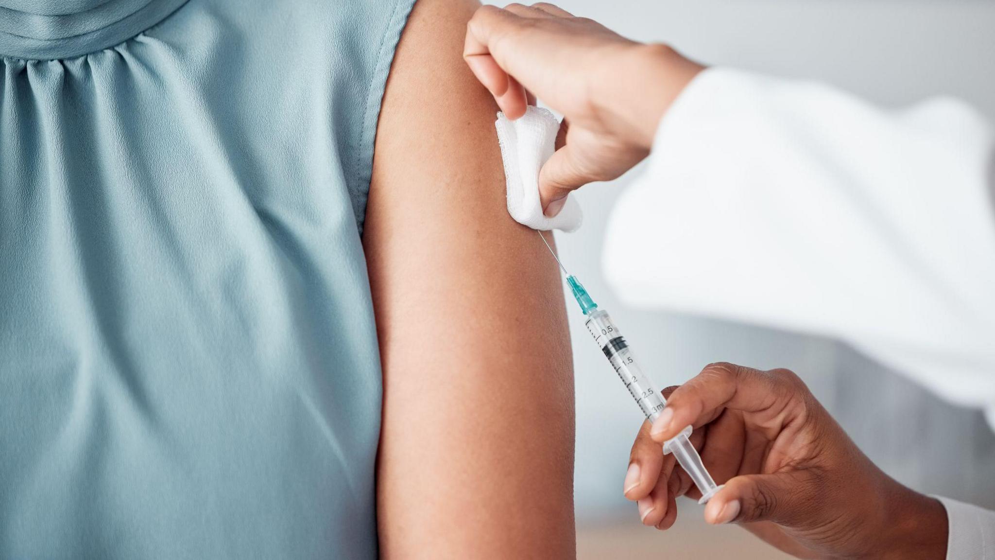 Woman in a blue silk sleeveless job receiving an injection from a medical professional