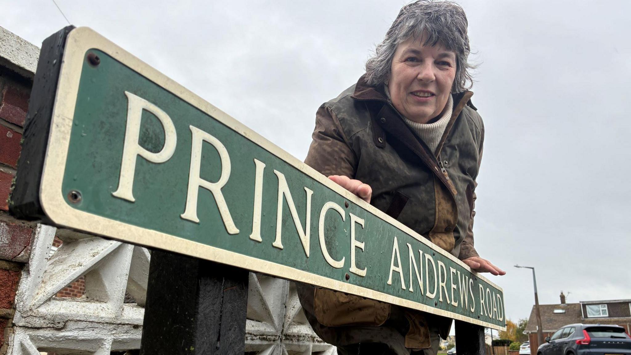 Shelagh Gurney leans over a sign saying St Andrews Road. 