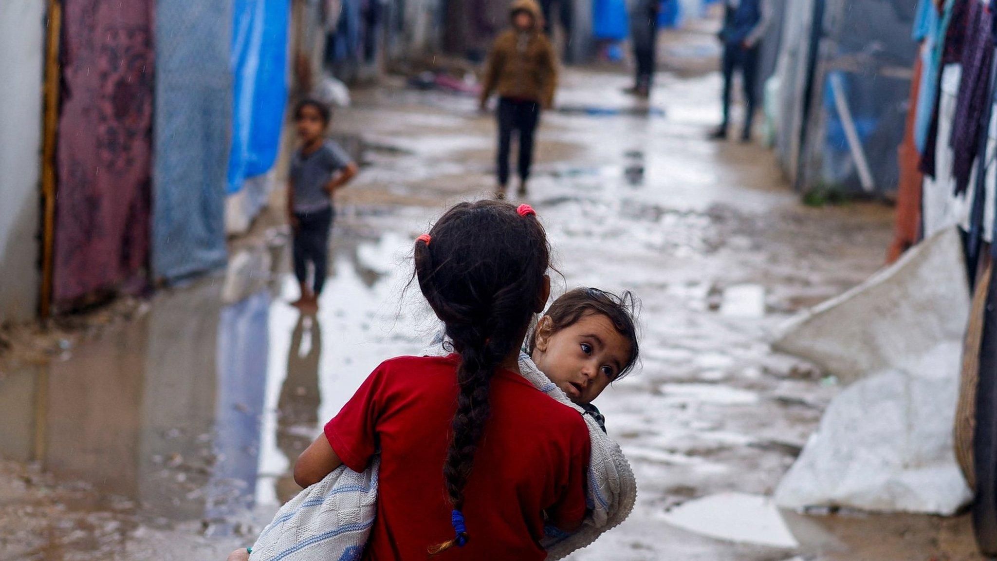 A Palestinian girl carries a baby at a camp for displaced people in Rafah, in the southern Gaza Strip (6 May 2024)