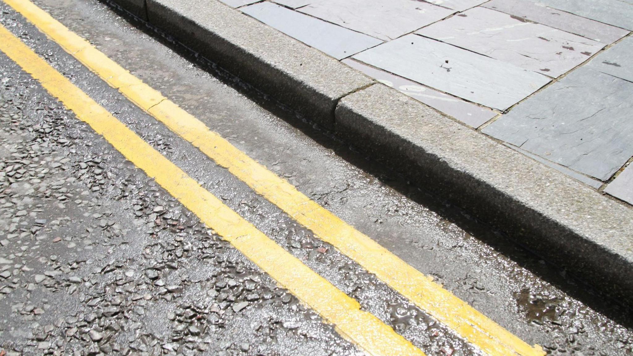 A close-up of double yellow lines on a wet road.