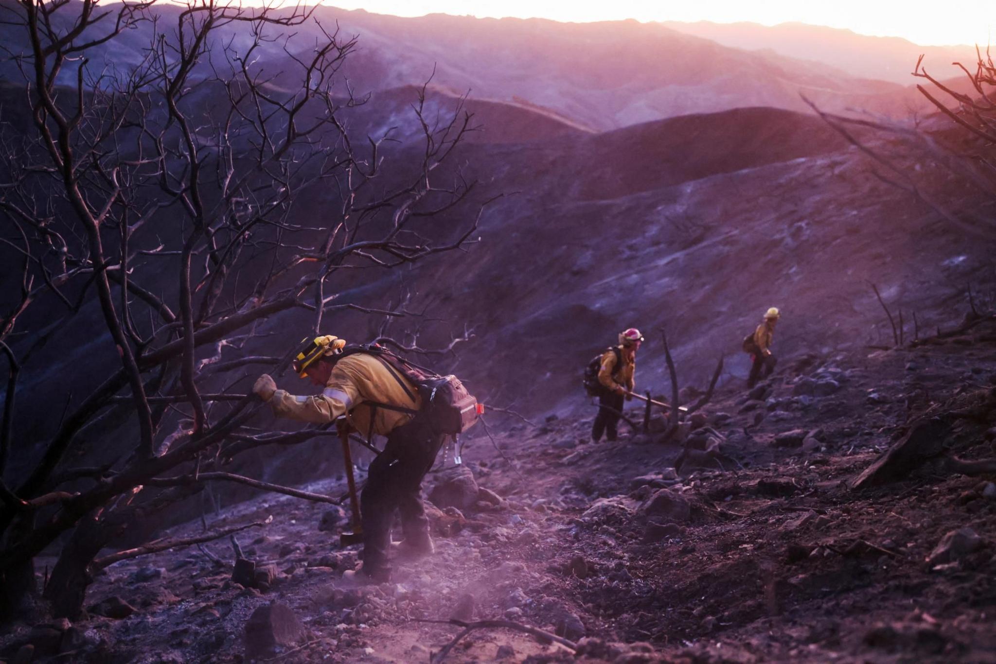 Three firefighters work to put out any remaining embers in a charred landscape n LA 