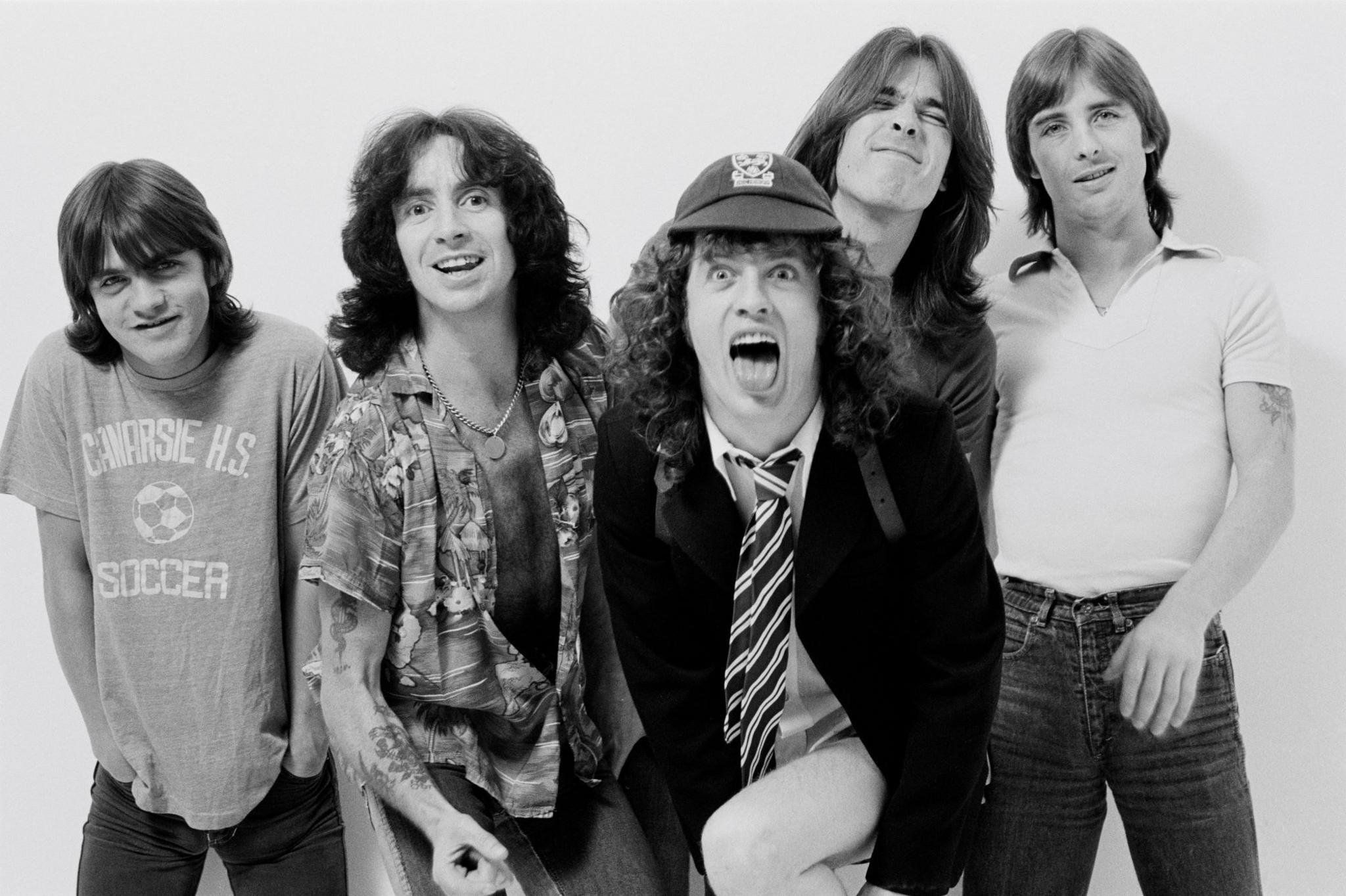 AC/DC IN 1979 - from L-R Malcolm Young, Bon Scott, Angus Young, Cliff Williams and Phil Rudd. The group pose in a black and white promotional photo, all looking into the camera and smiling or making faces.