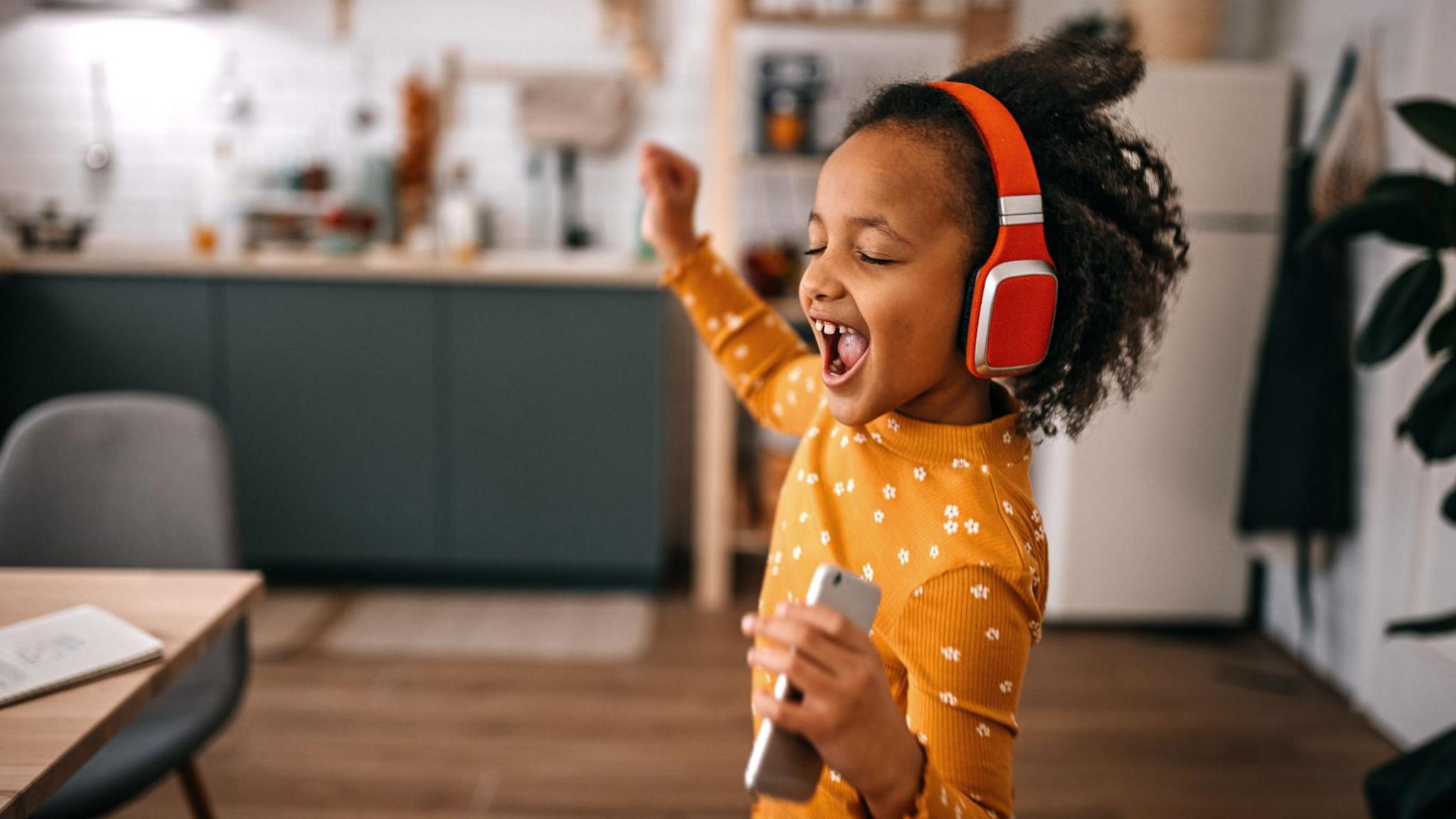 a child in a yellow top with white flowers listening to music and dancing wearing red headphones.