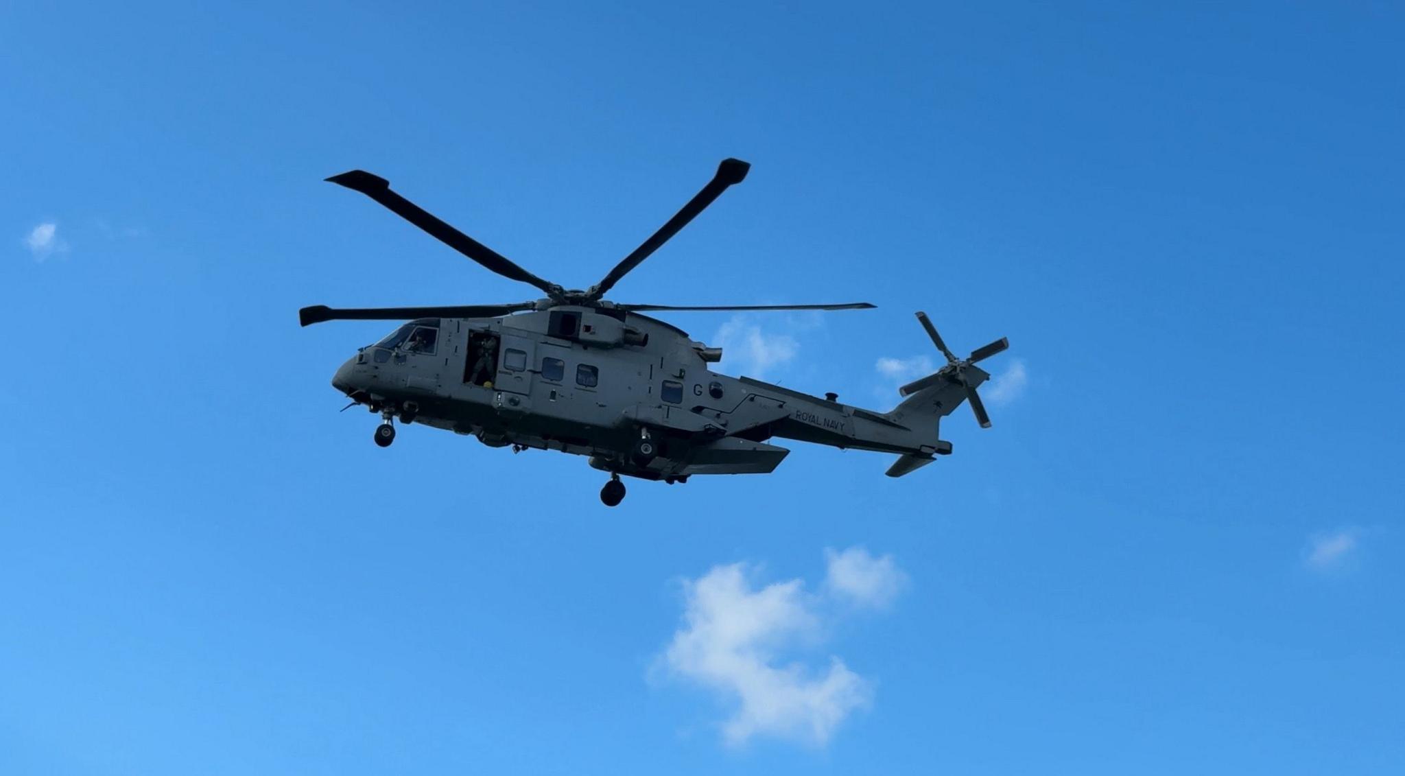 A grey Royal Navy MK4 helicopters in a clear, almost-cloudless sky.