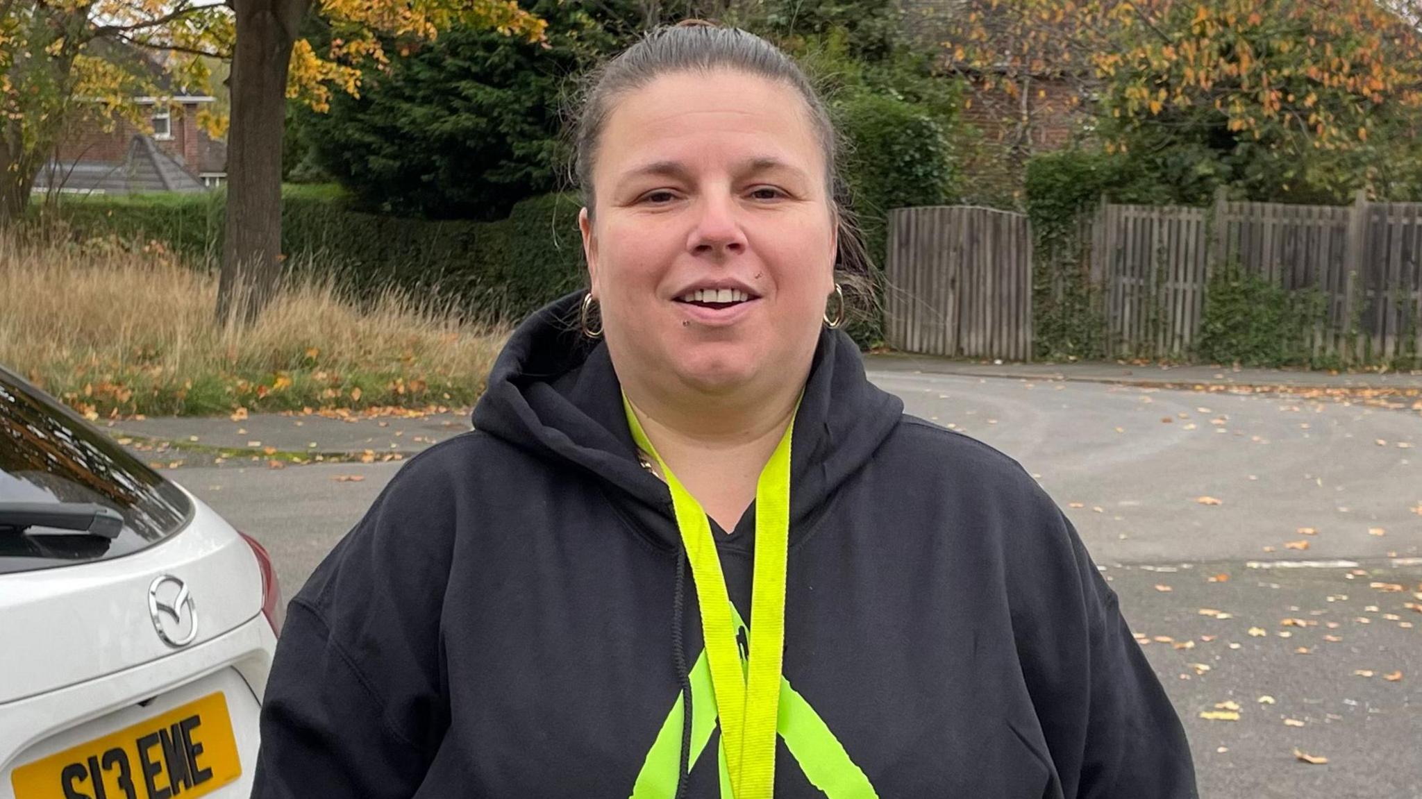 Zoe is stood in the street smiling, wearing a branded 'Always An Alternative' hoodie.