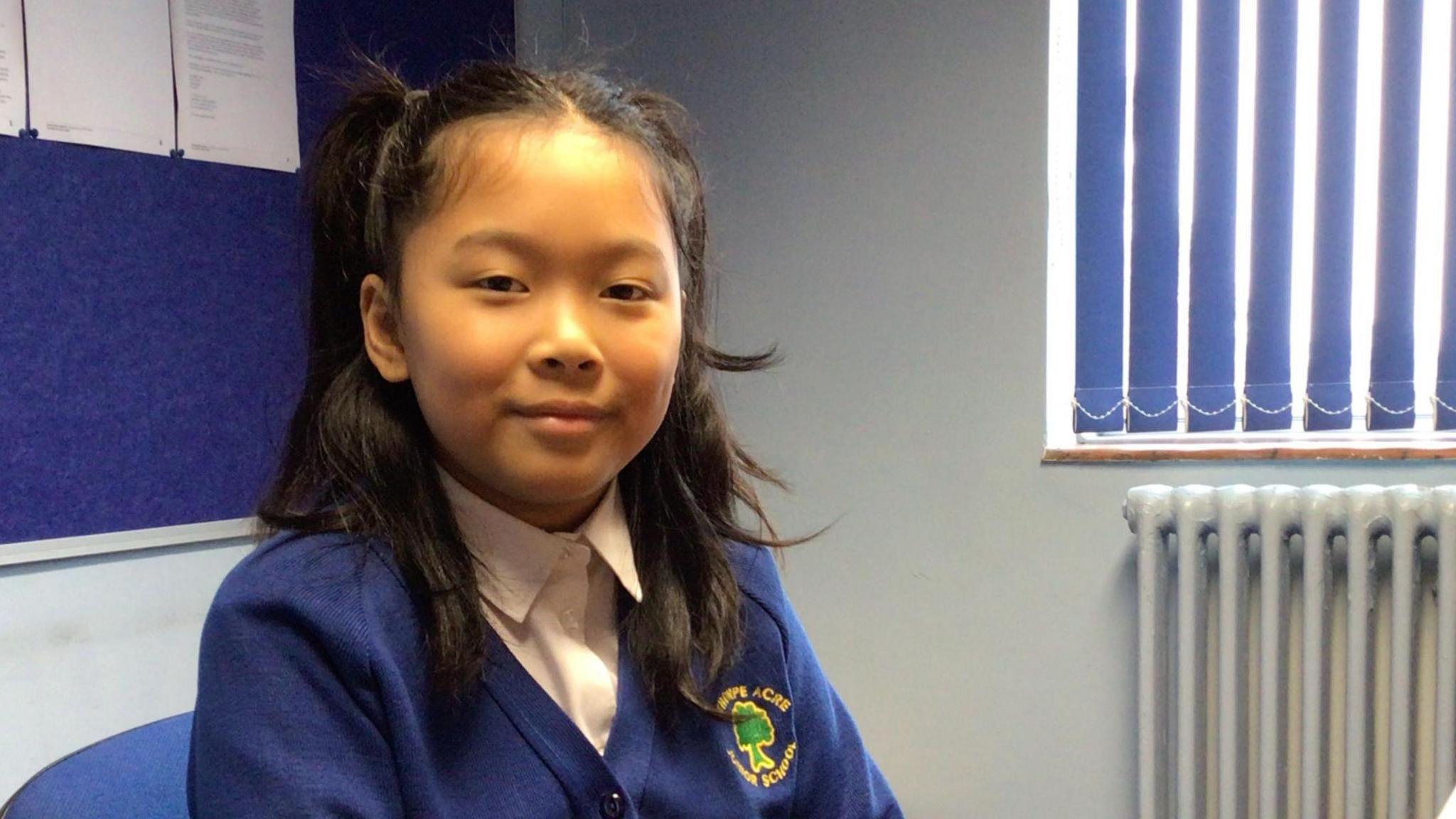 A smiling schoolgirl in her uniform sat at a desk