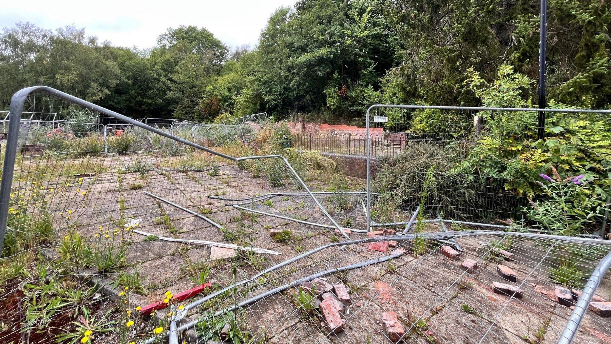 Metal fences, some of which are on the ground or at an angle. There are bricks on a path and trees in the background.