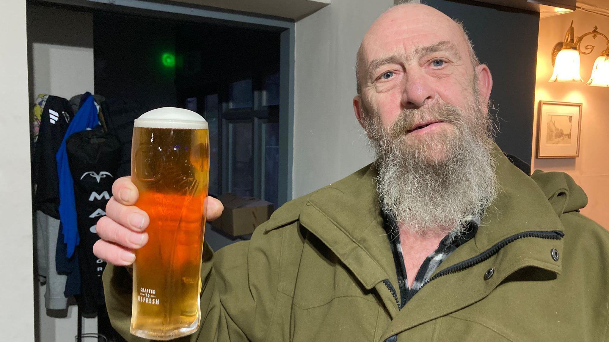 Paul Tylee-Hinder wearing a green coat while holding a pint of beer and looking into the camera.