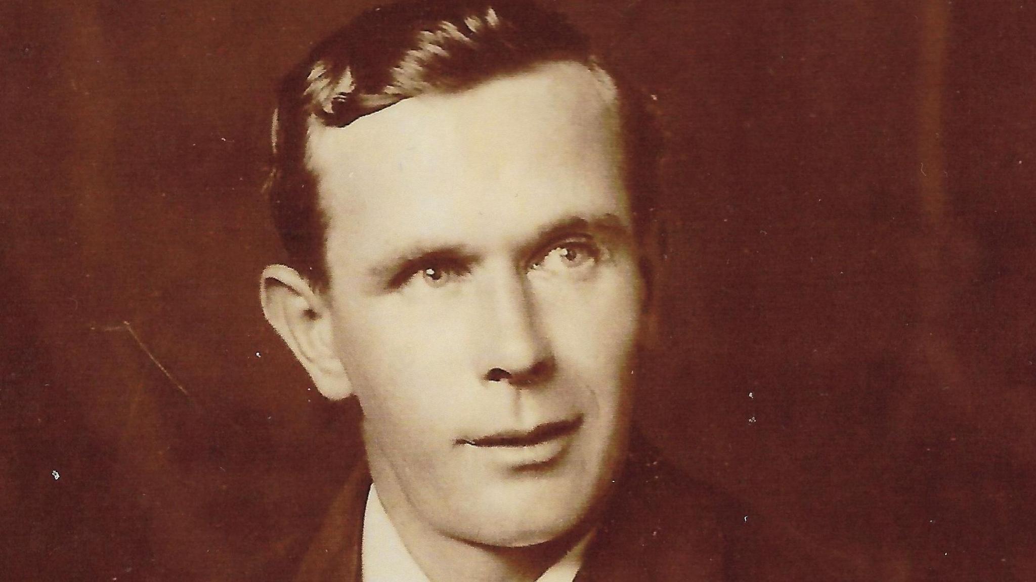 Black and white photo of Mr Barker. He is looking to the right side of the camera and has dark, slicked back hair.