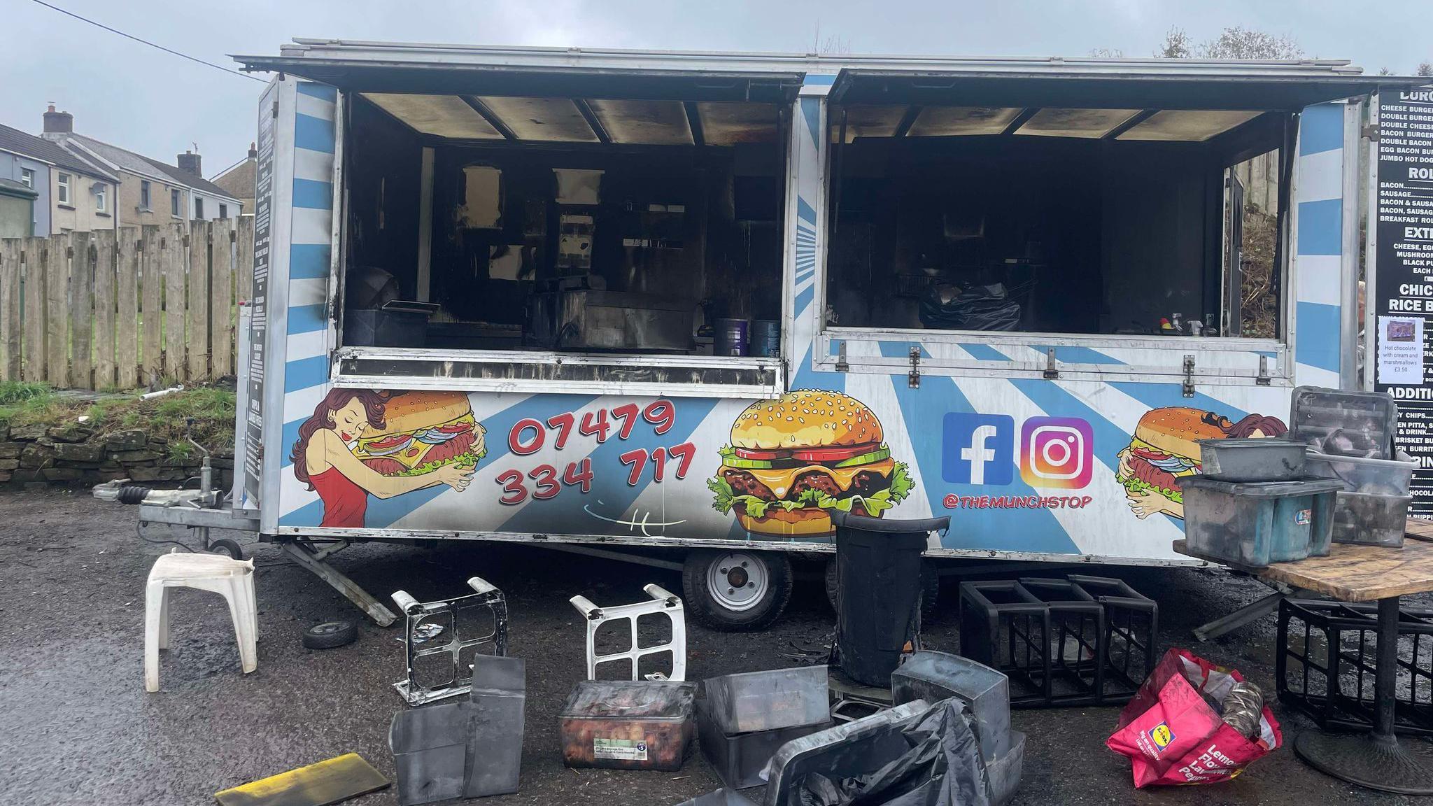 Jordan's burger van from the outside with burn marks visible and equipment from the van strewn on the floor 