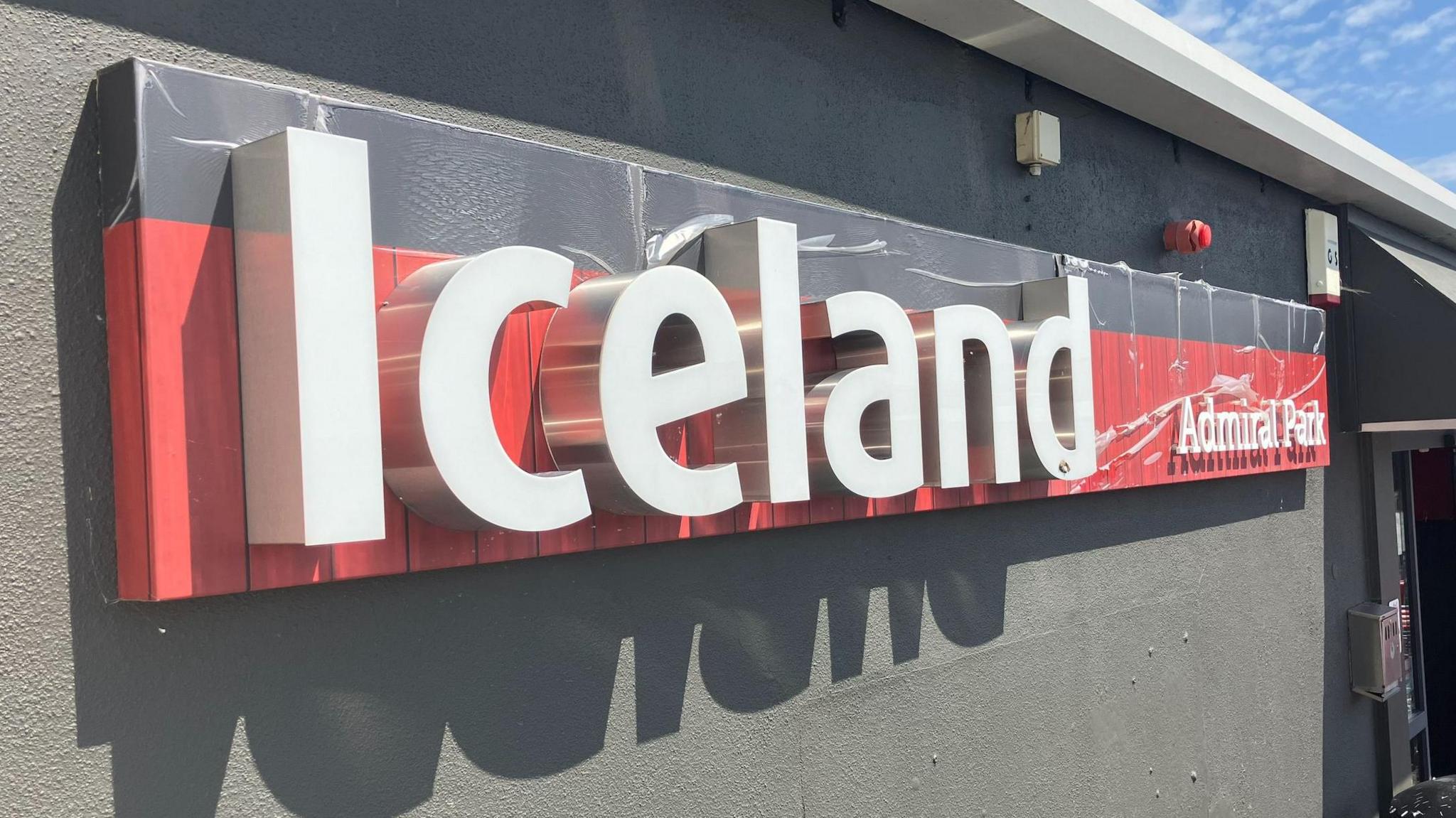 The Iceland shop logo. The background is red, with white text on top which reads 'Iceland' and 'Admiral Park'.