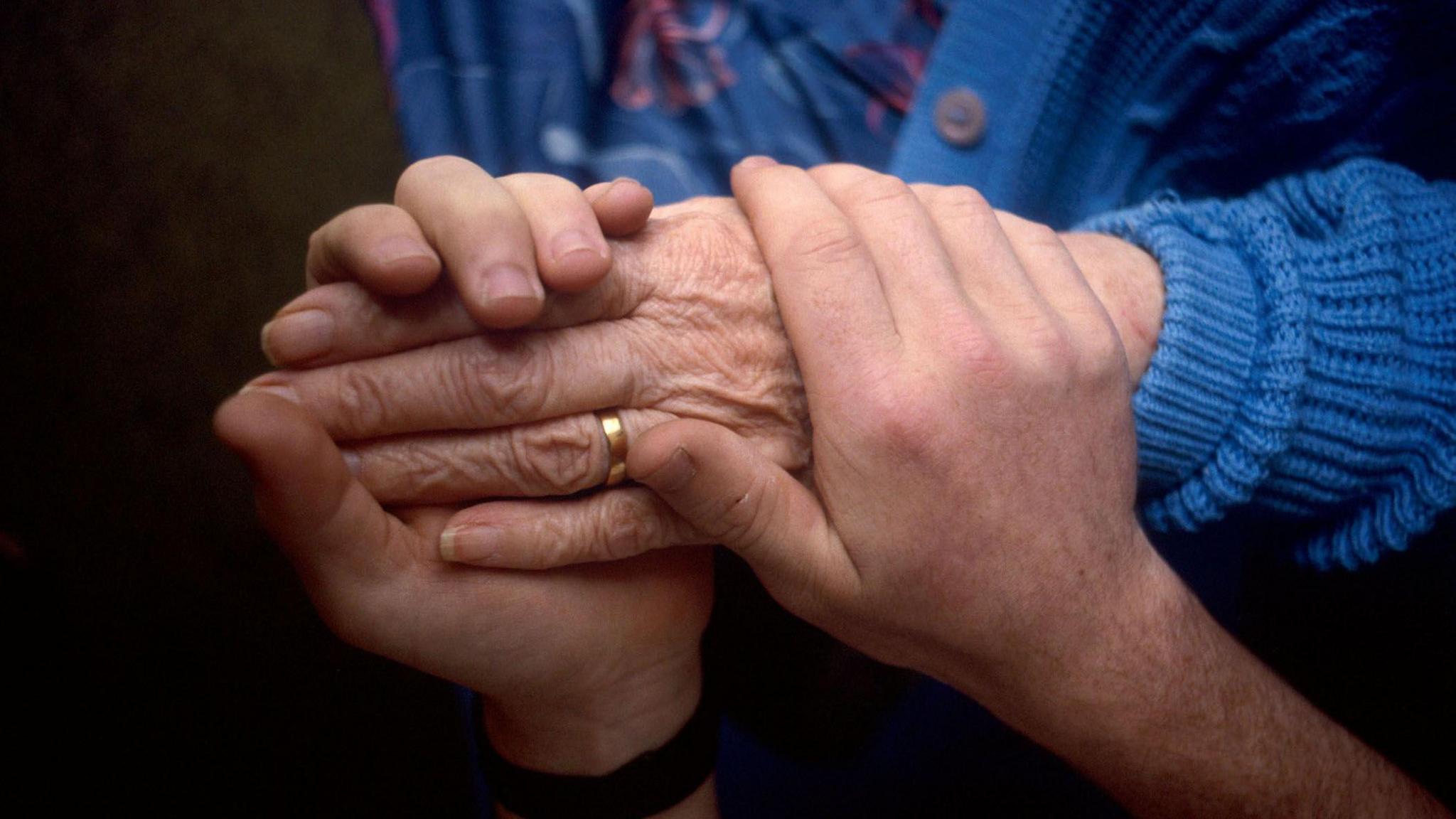 A stock image showing a close up of a carer holding the hand of an elderly person.