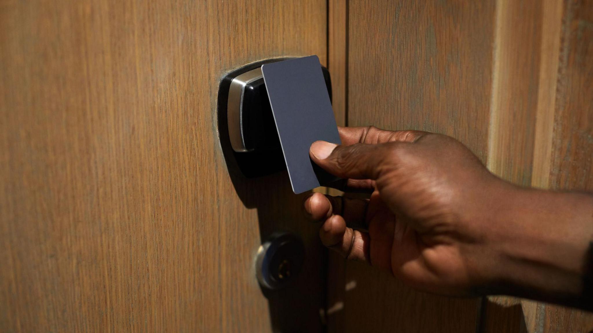 A hand holding a key card up to a hotel room door