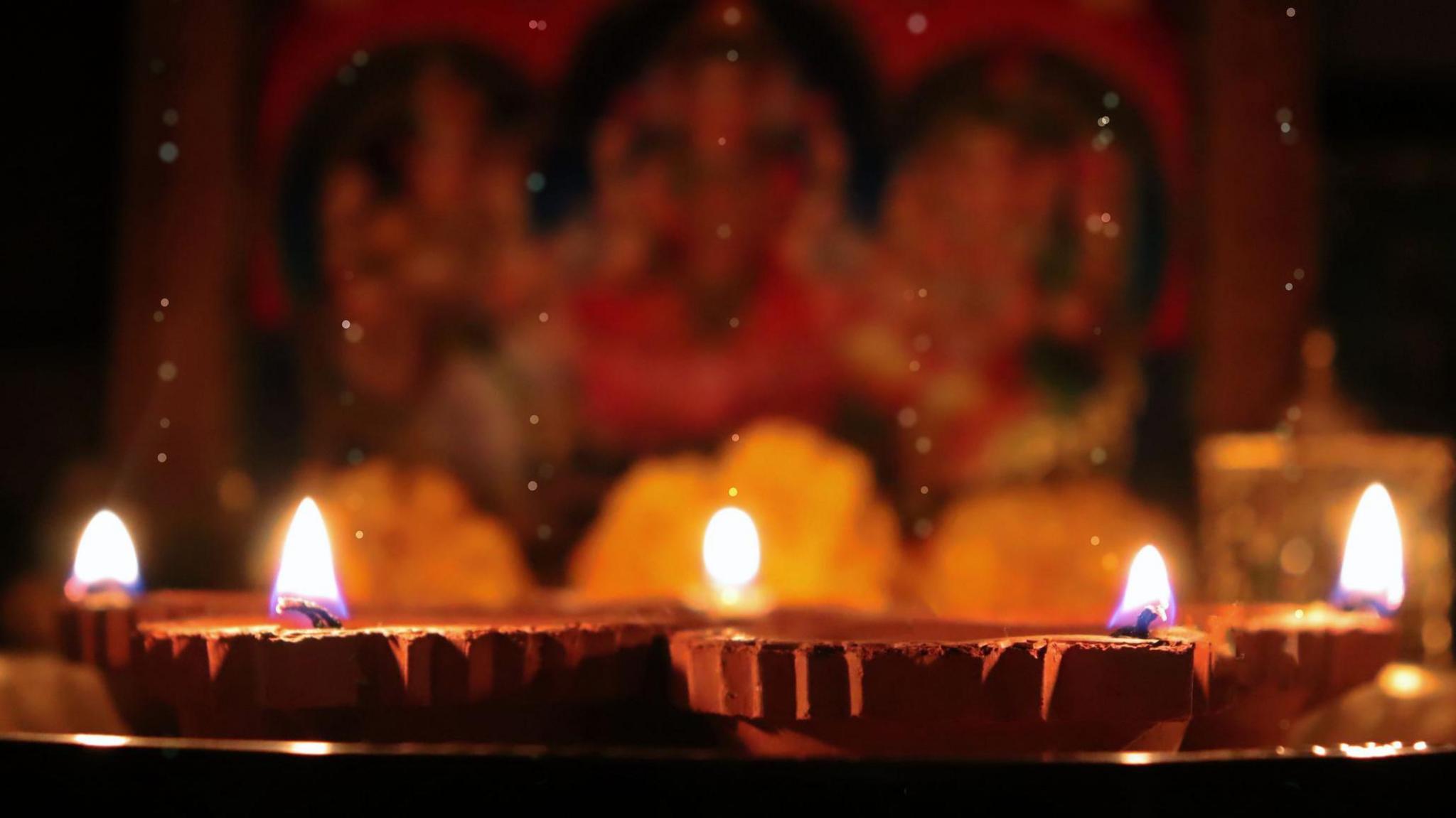 An arrangement of small clay oil lamps sit in front of a religious painting.