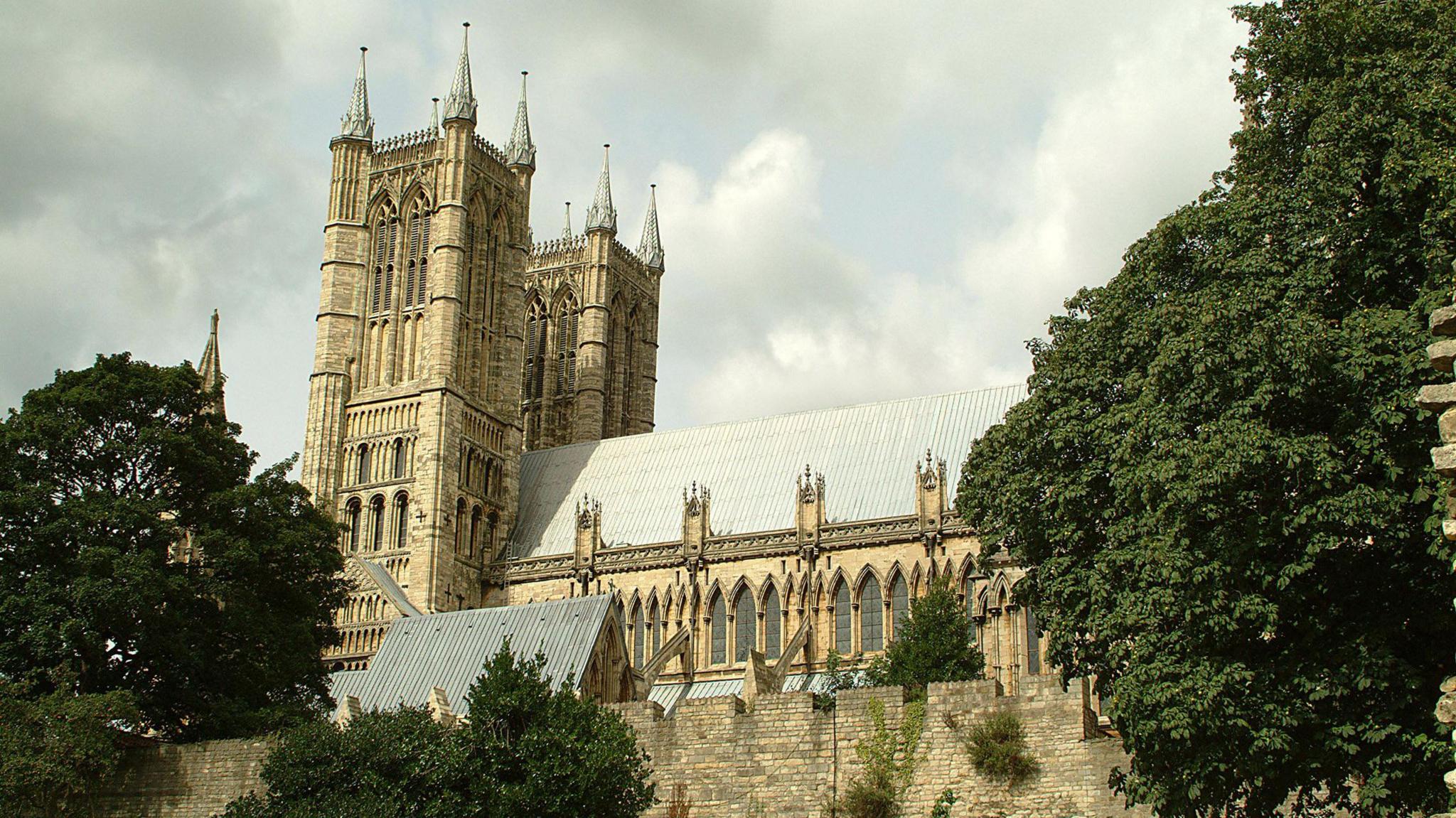 The building captured from a side angle (in landscape view). The two ornate towers are to the left of the picture and the rest of the building with its grey roof stretches out behind the towers. The building is surrounded by walls.