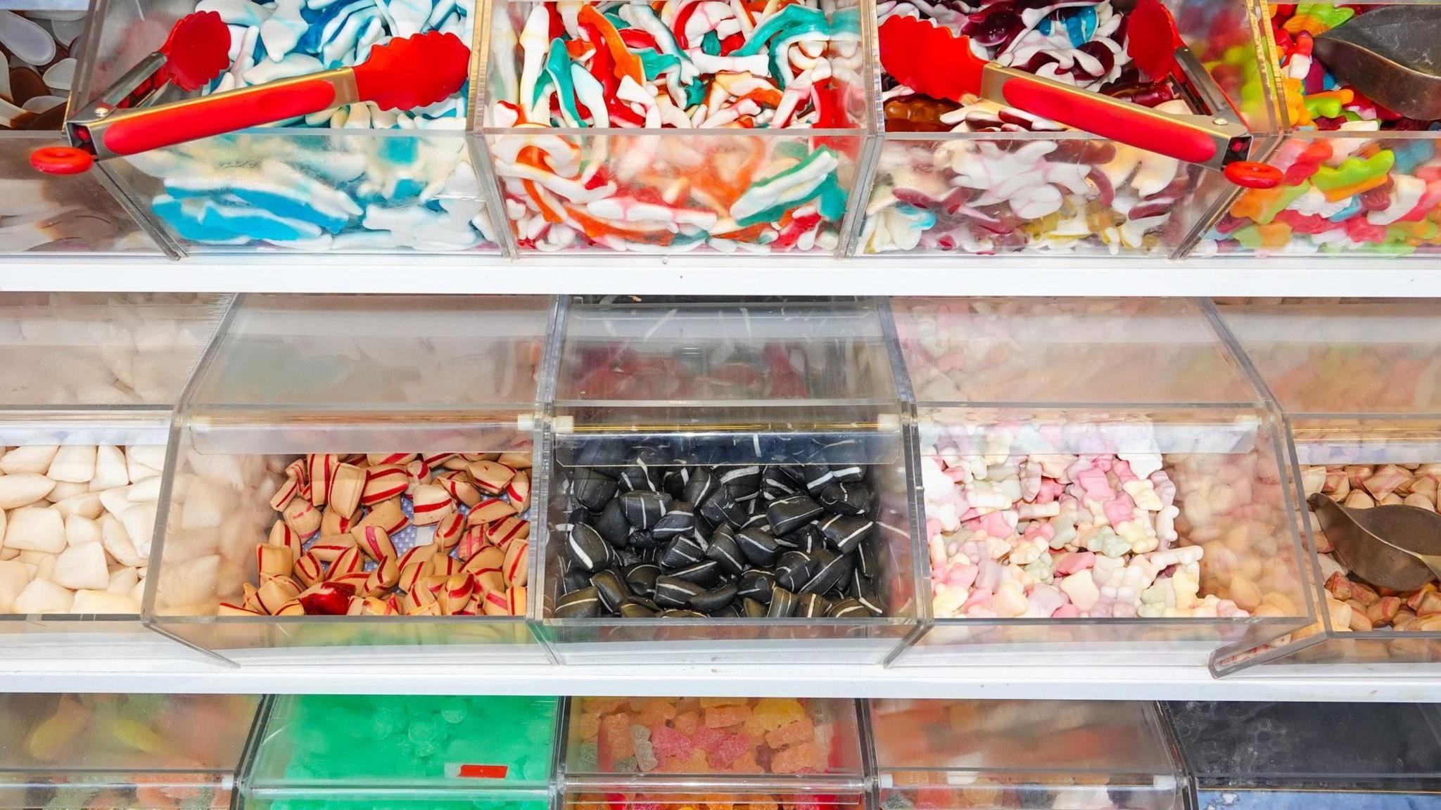 Boxes of sweets for a pick'n'mix, including two red-handled tongs, and on the right of the picture, two metal sweet scoops