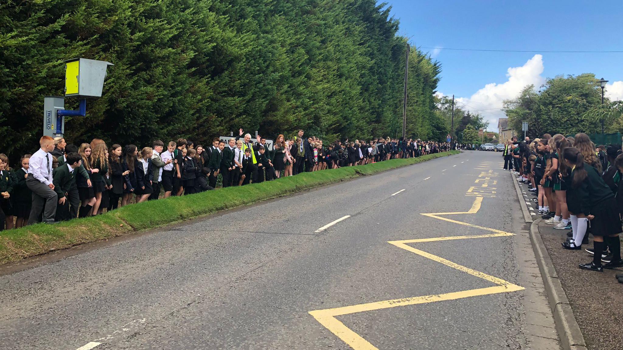 An empty road with children lining either side. There are tall 
