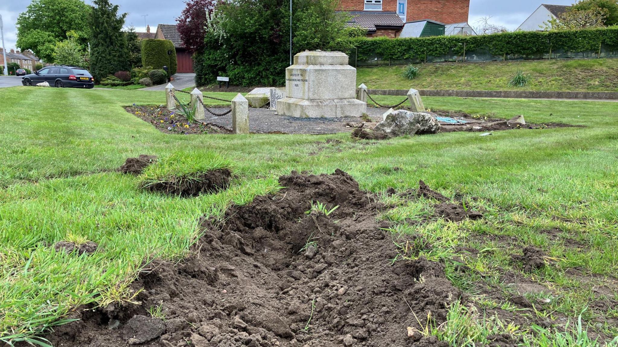 The damaged memorial, with turfed up grass in the foreground