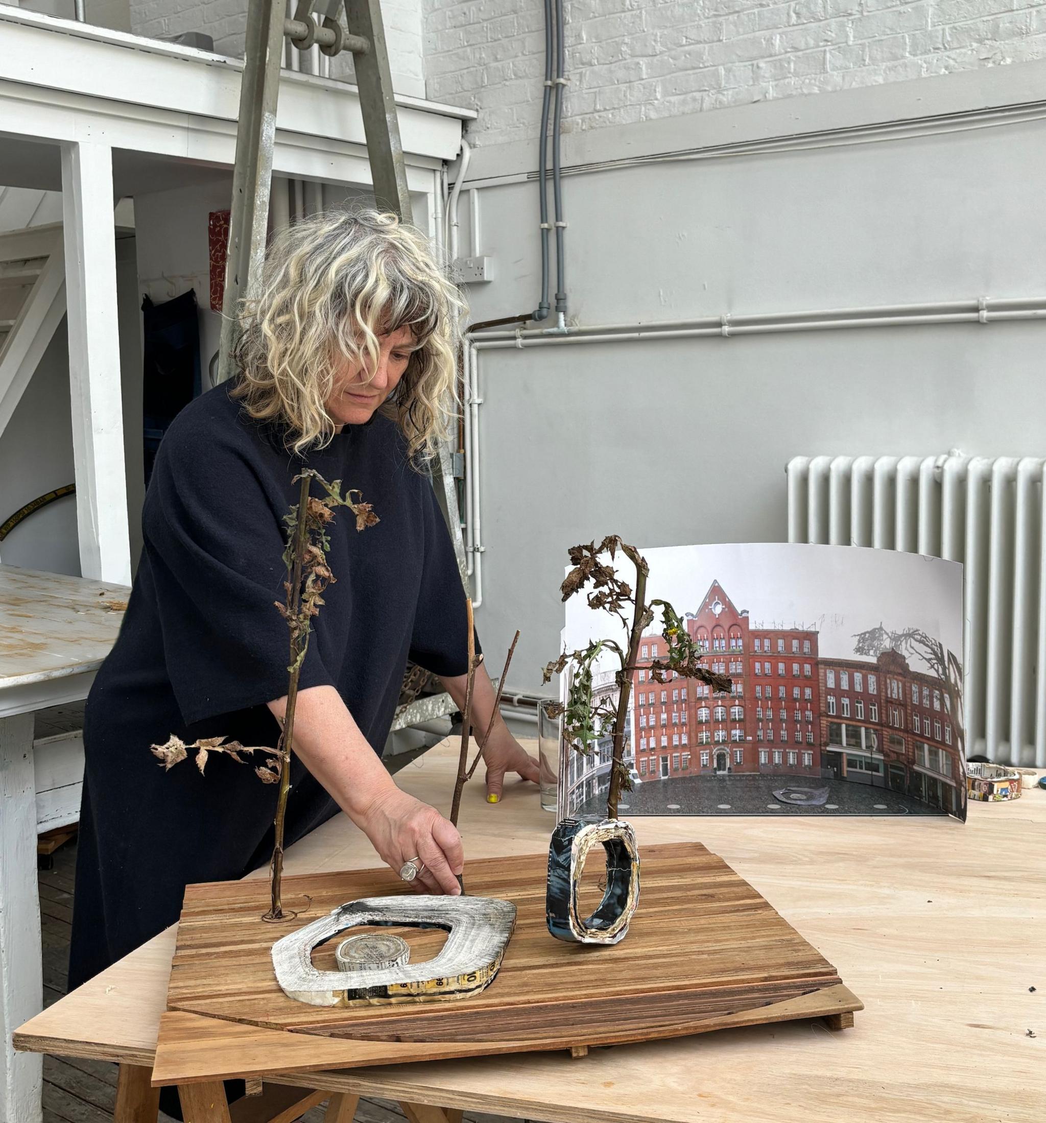 Artist with a mock-up of her design; it shows a tree trunk standing vertically and one to the left lying horizontally