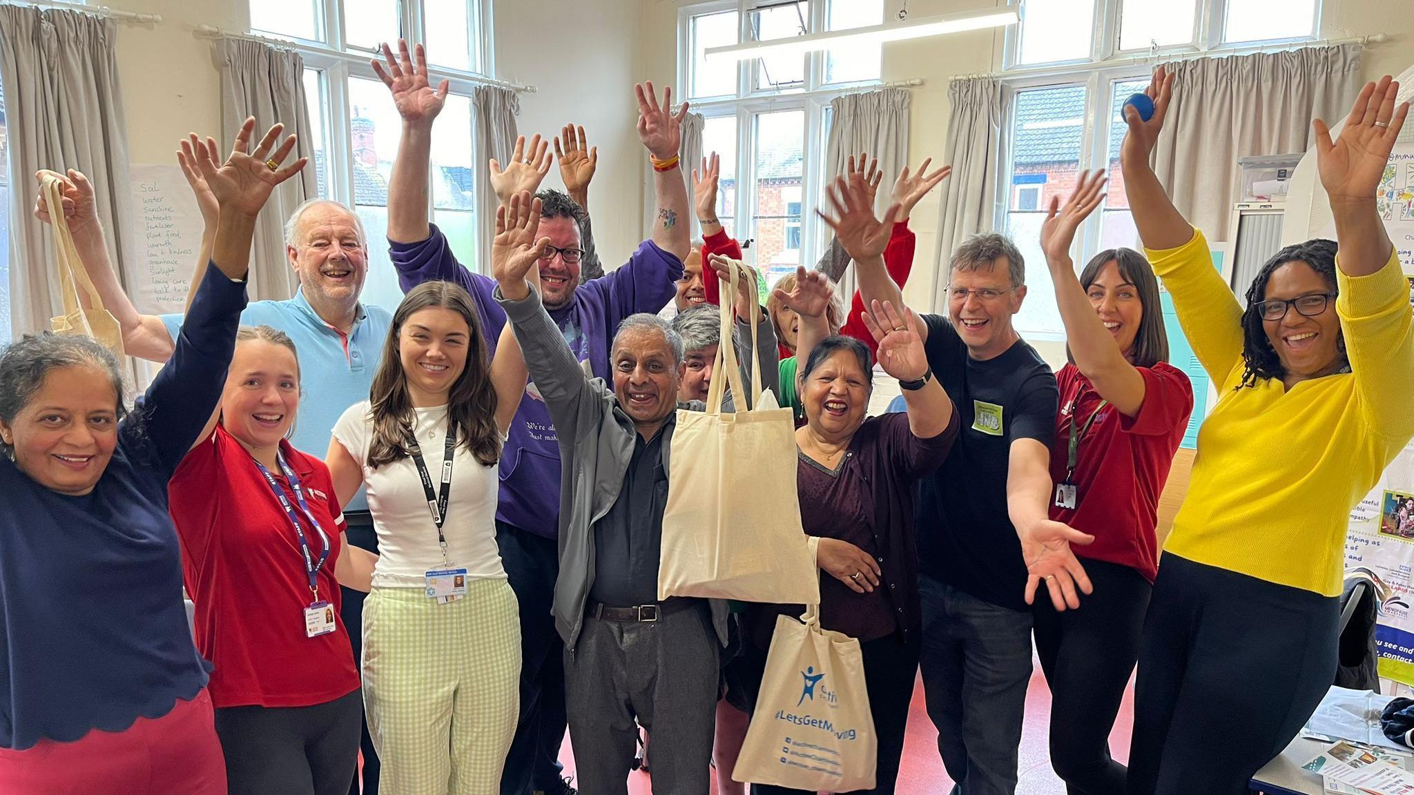 A group of patients, a GP, and fitness instructors cheering in a room at Fearon Hall, Loughborough 