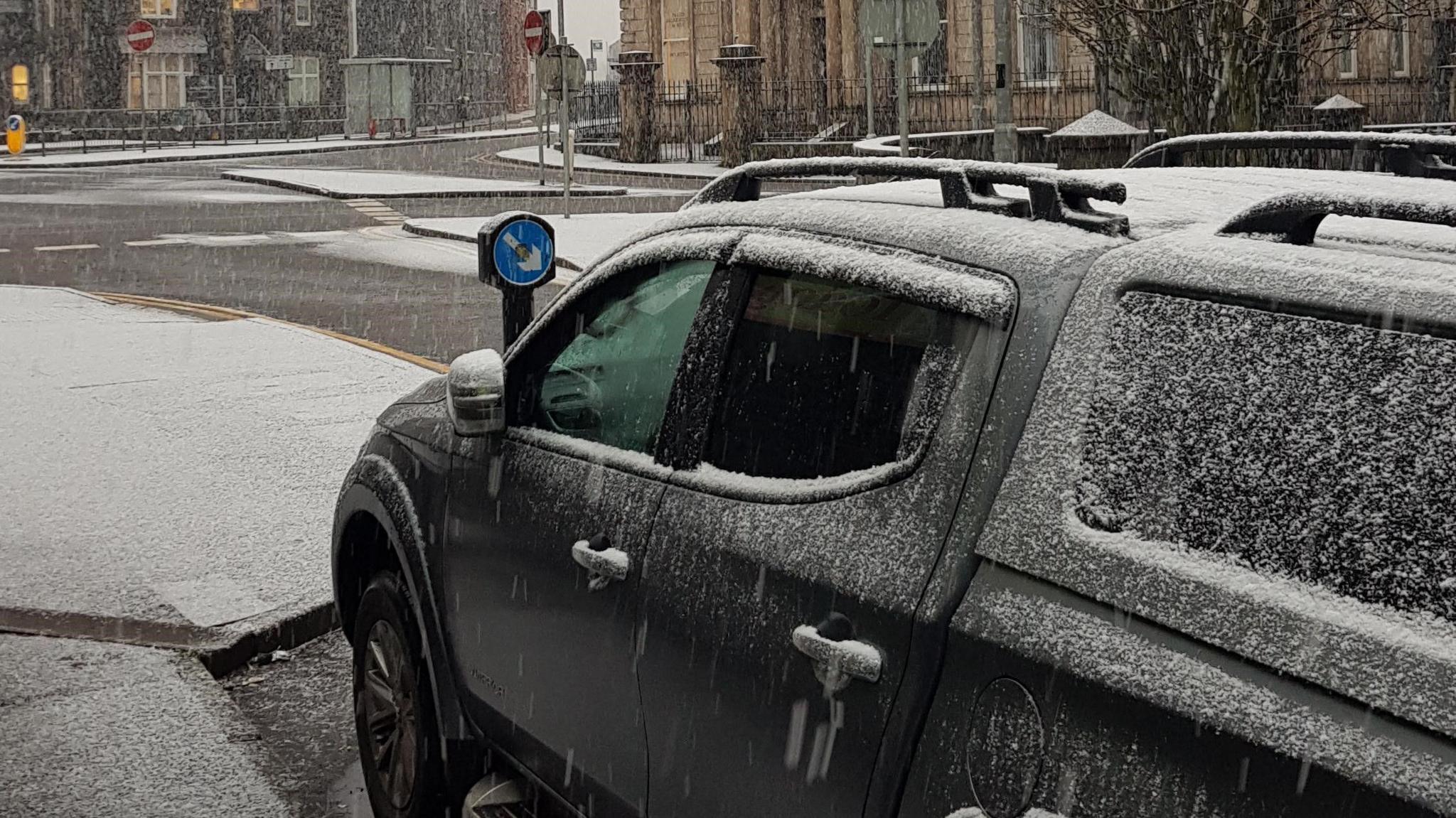 A black car covered in snow, parked on a snowy road. 