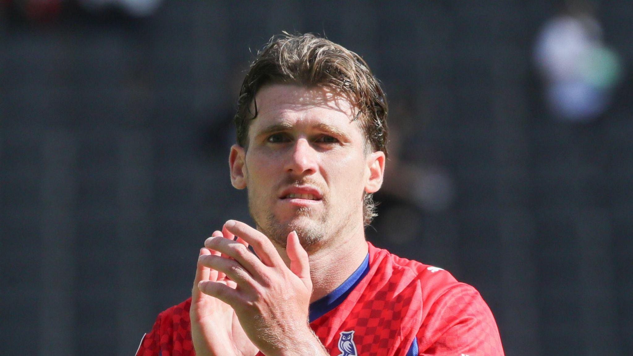 Reagan Ogle clapping Oldham fans at the end of a match wearing a red away kit