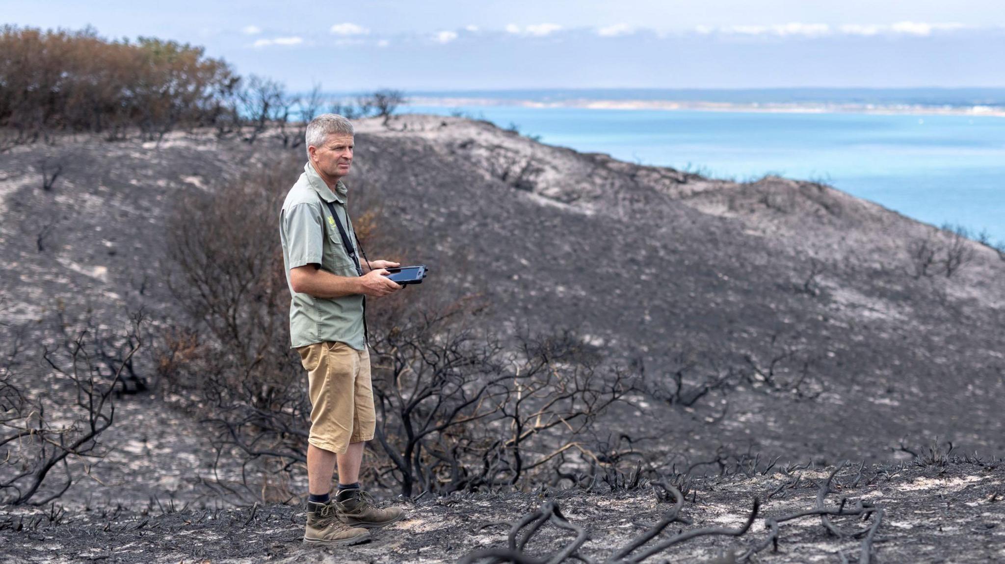 A man standing in a scorched heathland after a wild fire