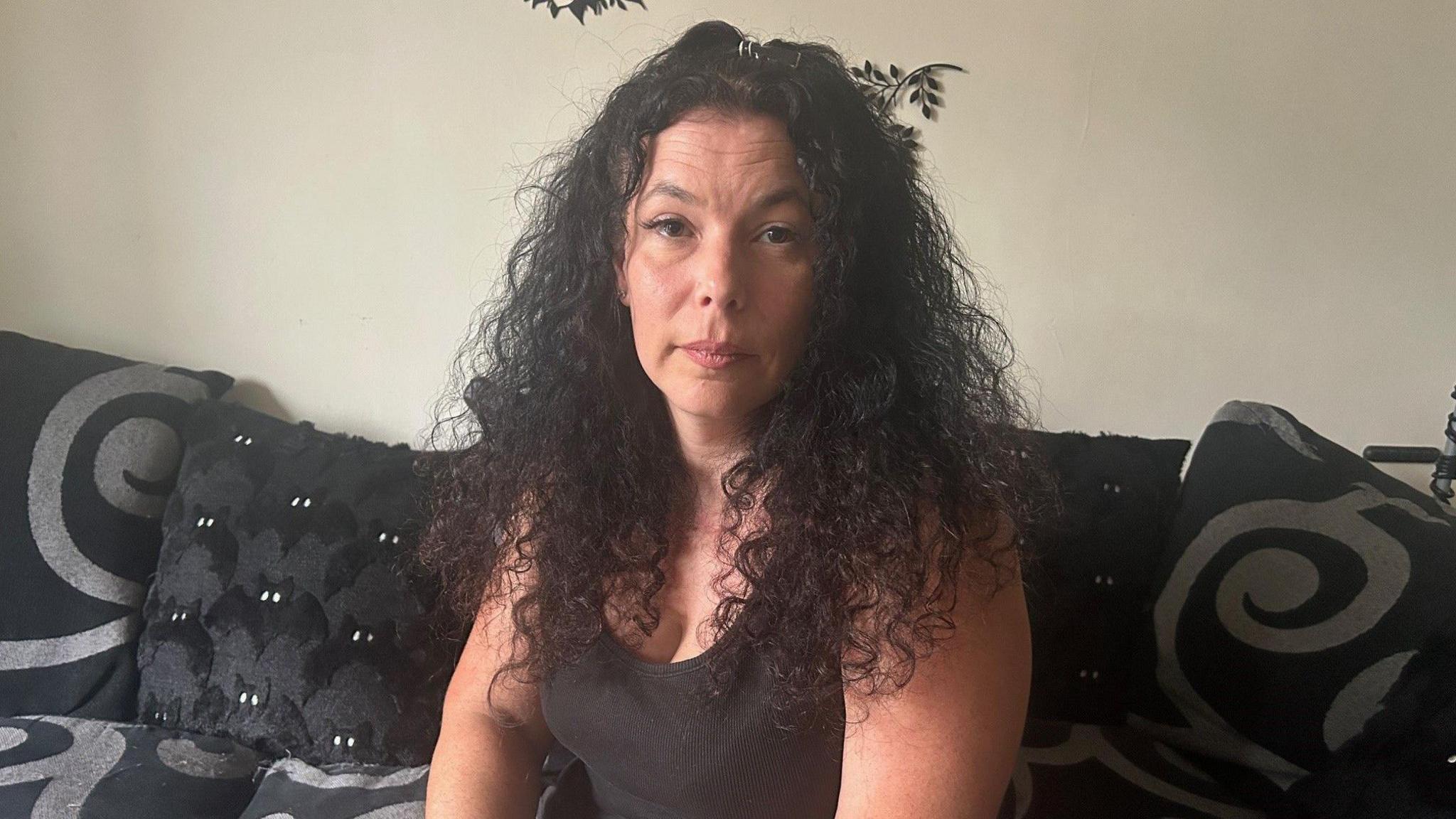 A woman with long dark curly hair sitting on a black and grey patterned sofa