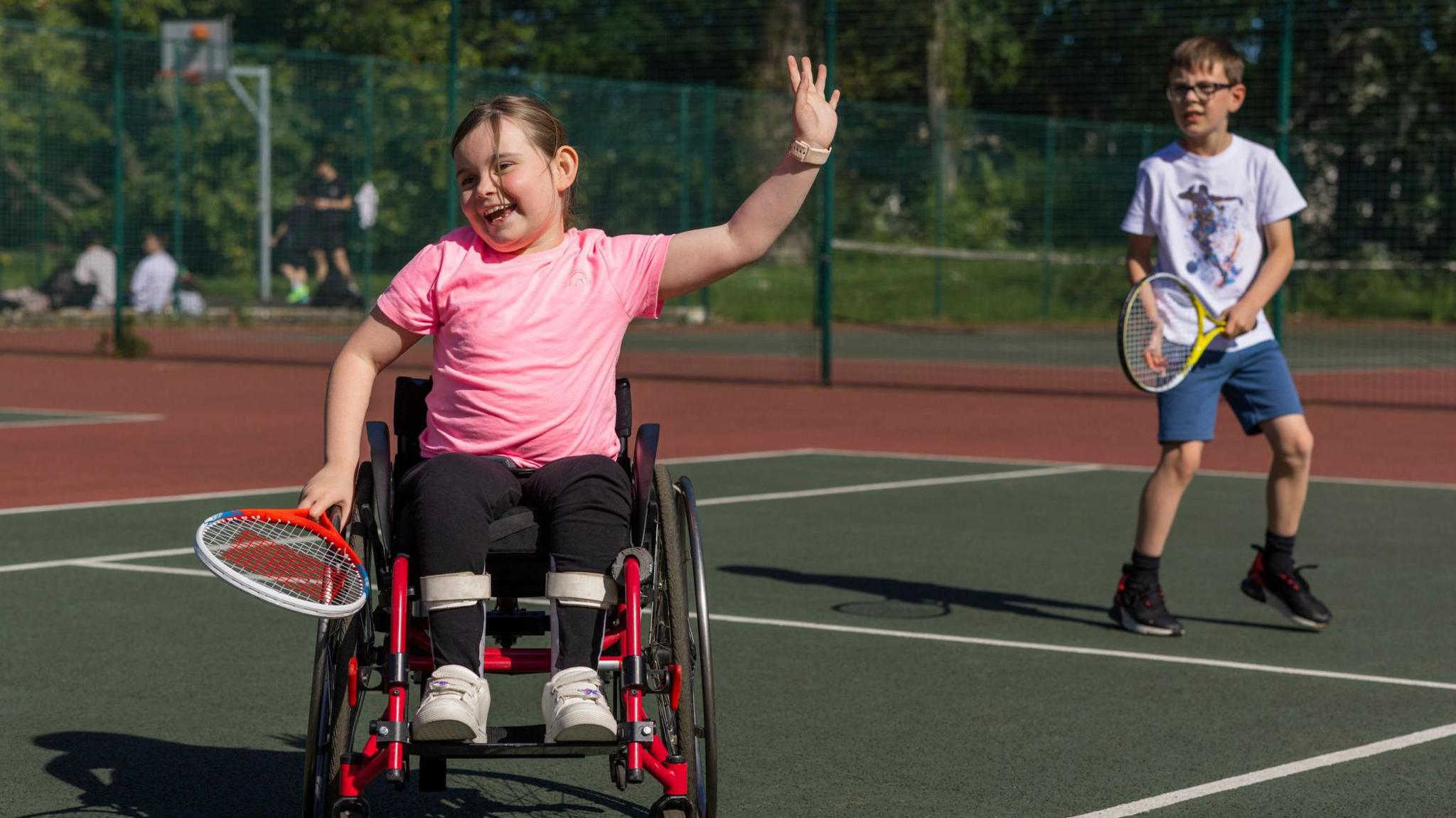 Two children playing tennis, including a girl in the foreground in a wheelchair.