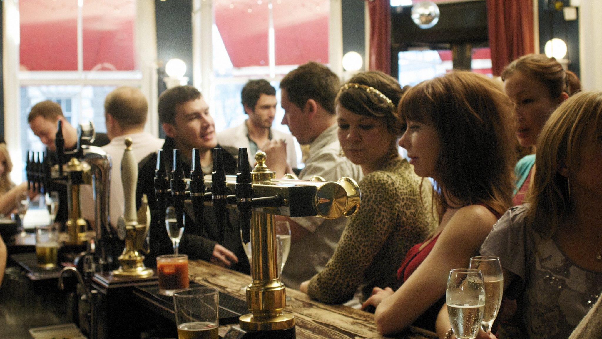 File image: People crowd around a bar in a pub in England