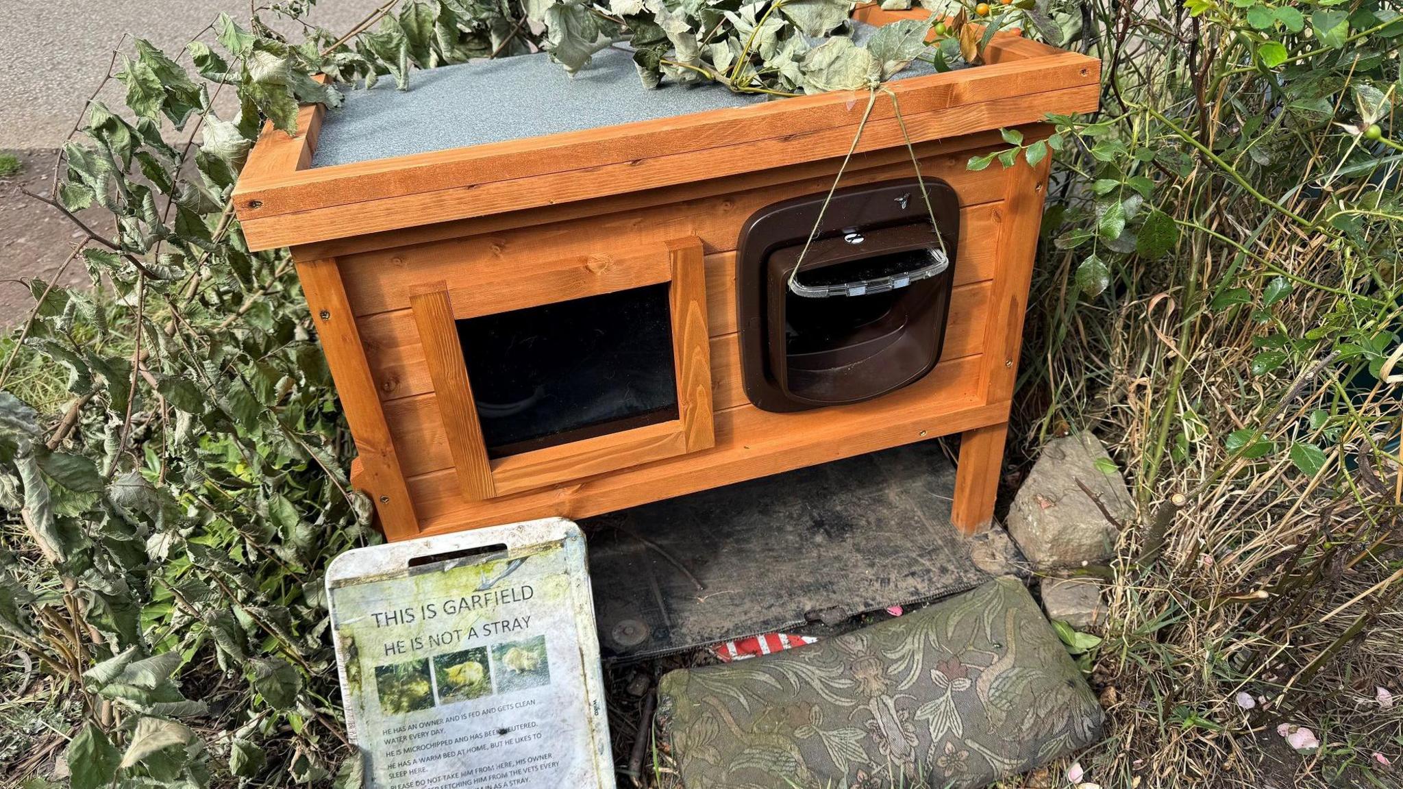 A wooden hutch surrounded by leaves and grass.