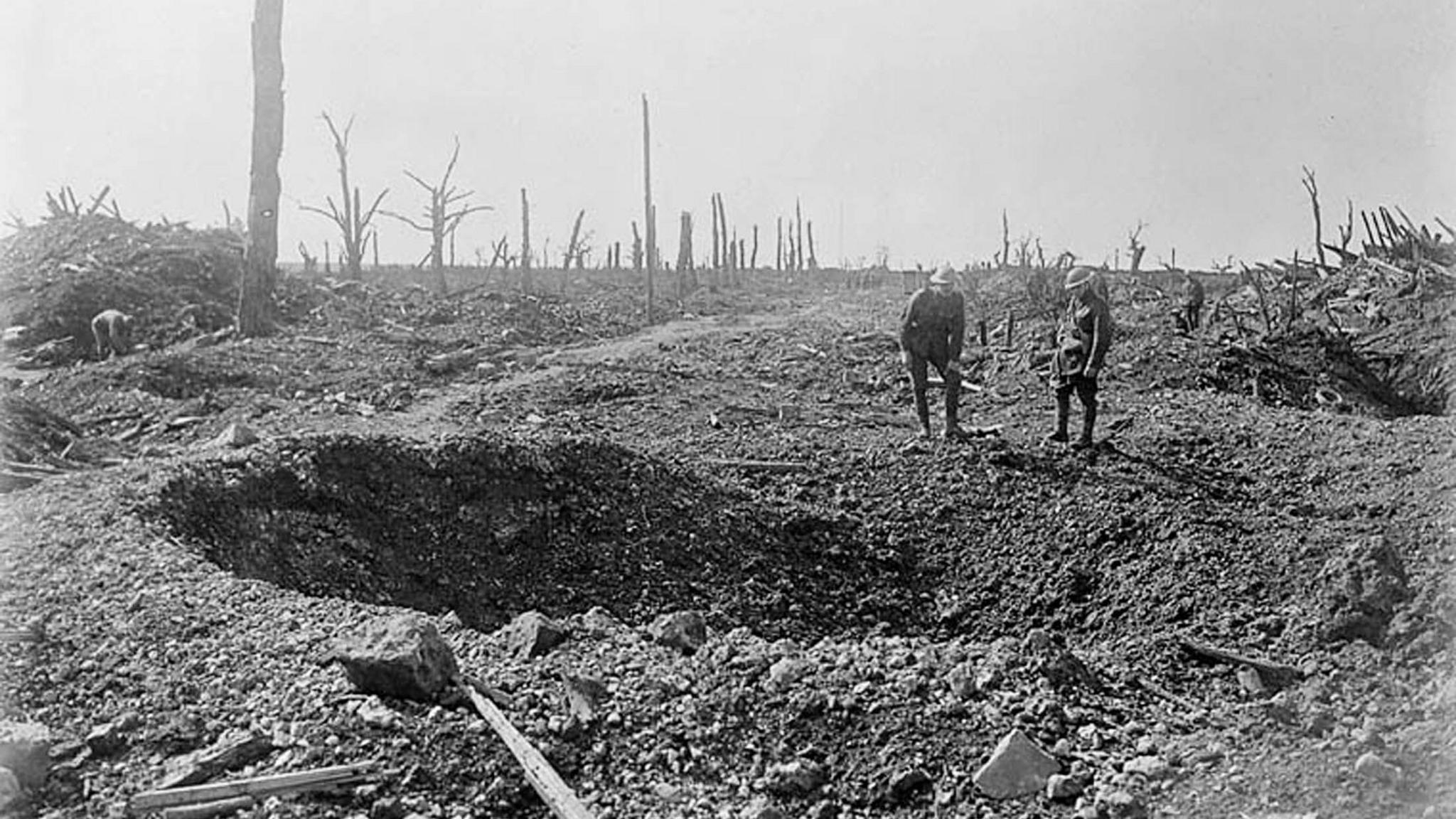 A black and white photograph of soldiers dwarfed by a shell crater on one of the roads to Bapaume during the Battle of the Somme, France in October 1916.