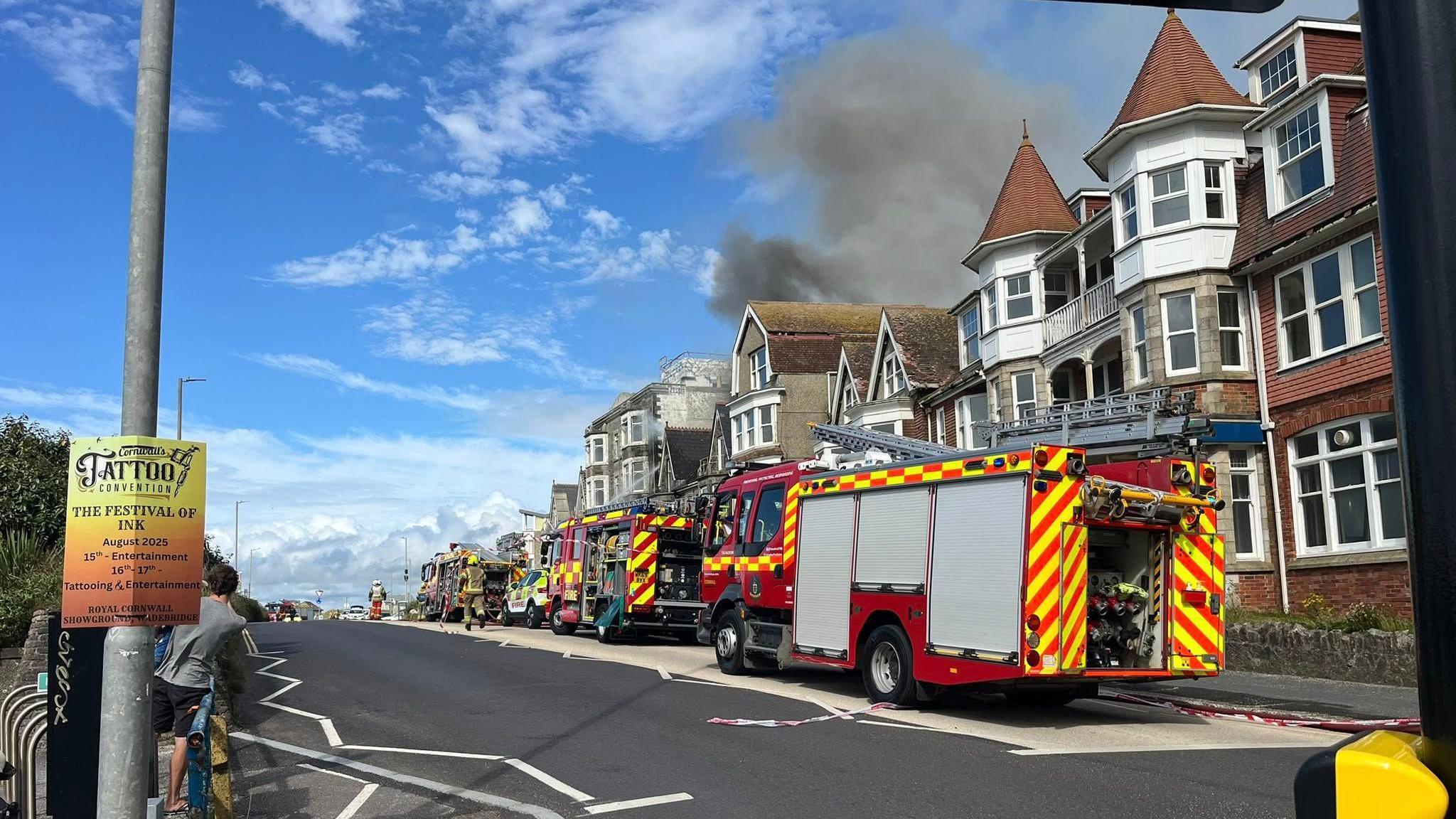 Smoke coming from the top of a building on fire, with fire engines in front of it