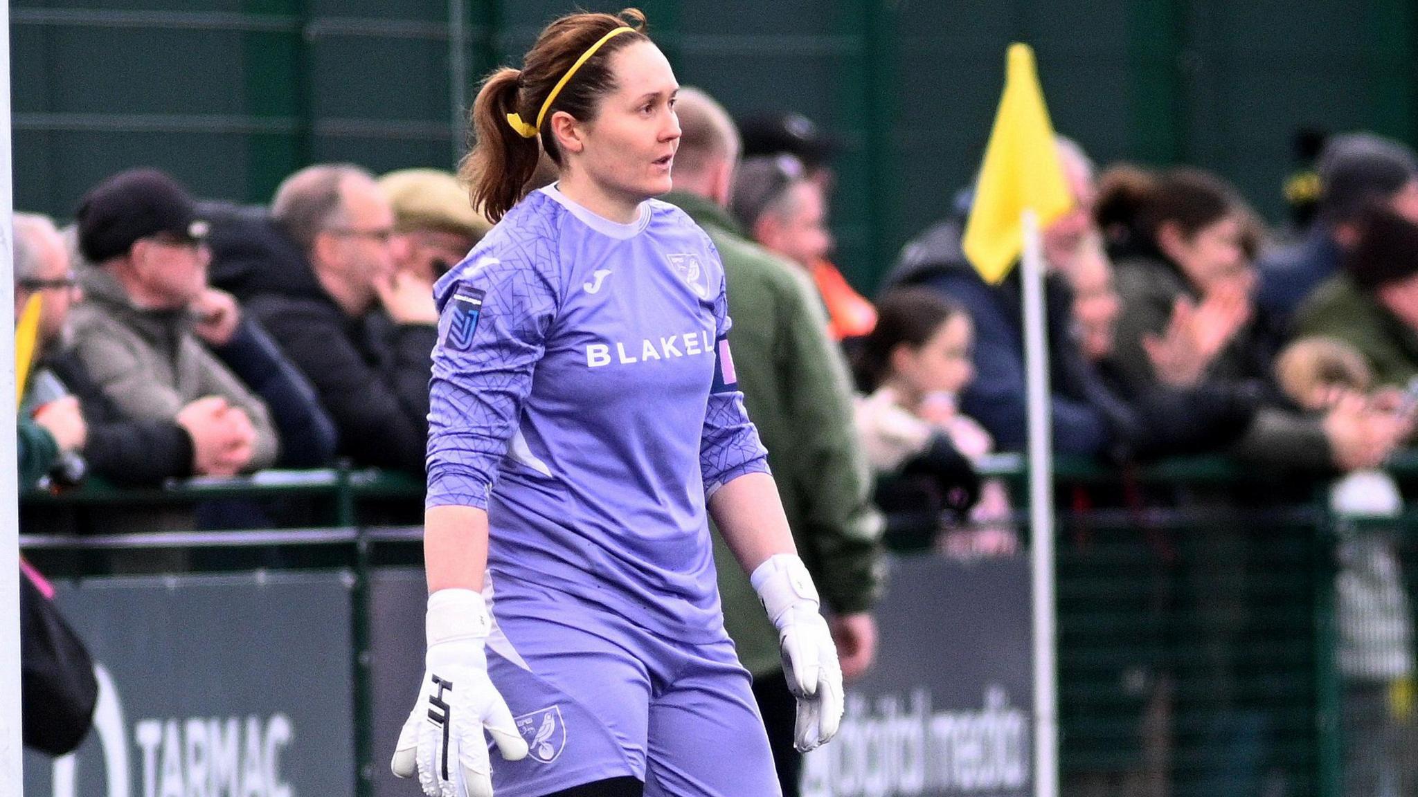 Sarah Quantrill, wearing a purple Norwich City Women's goalkeeper's kit, stands in her penalty area during a match