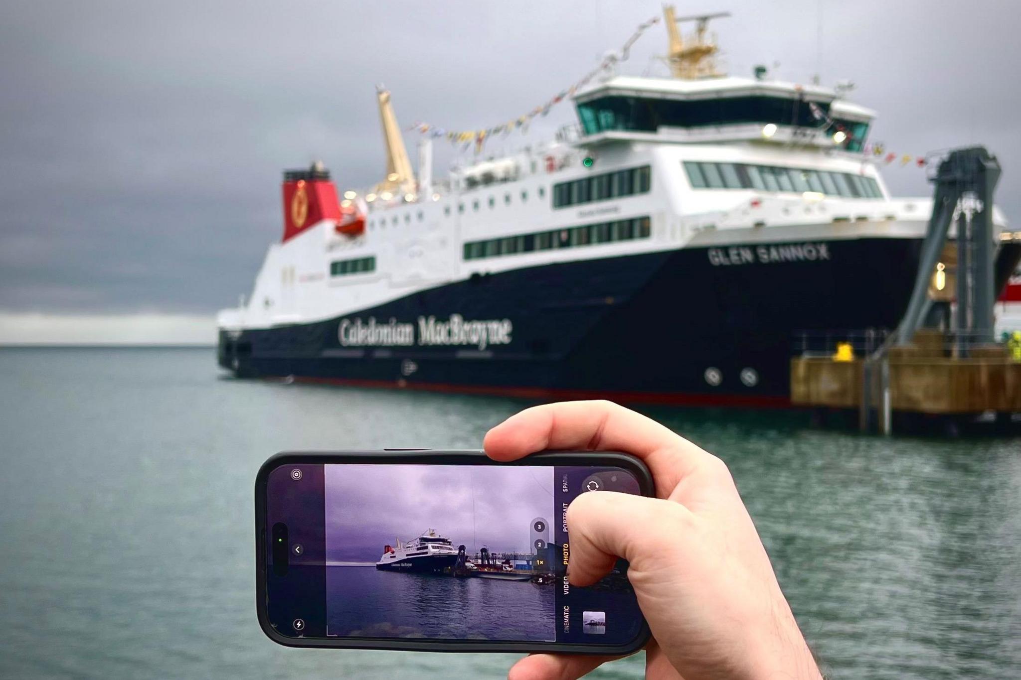 The ferry is berthed and a person is taking a picture of it using a mobile phone.