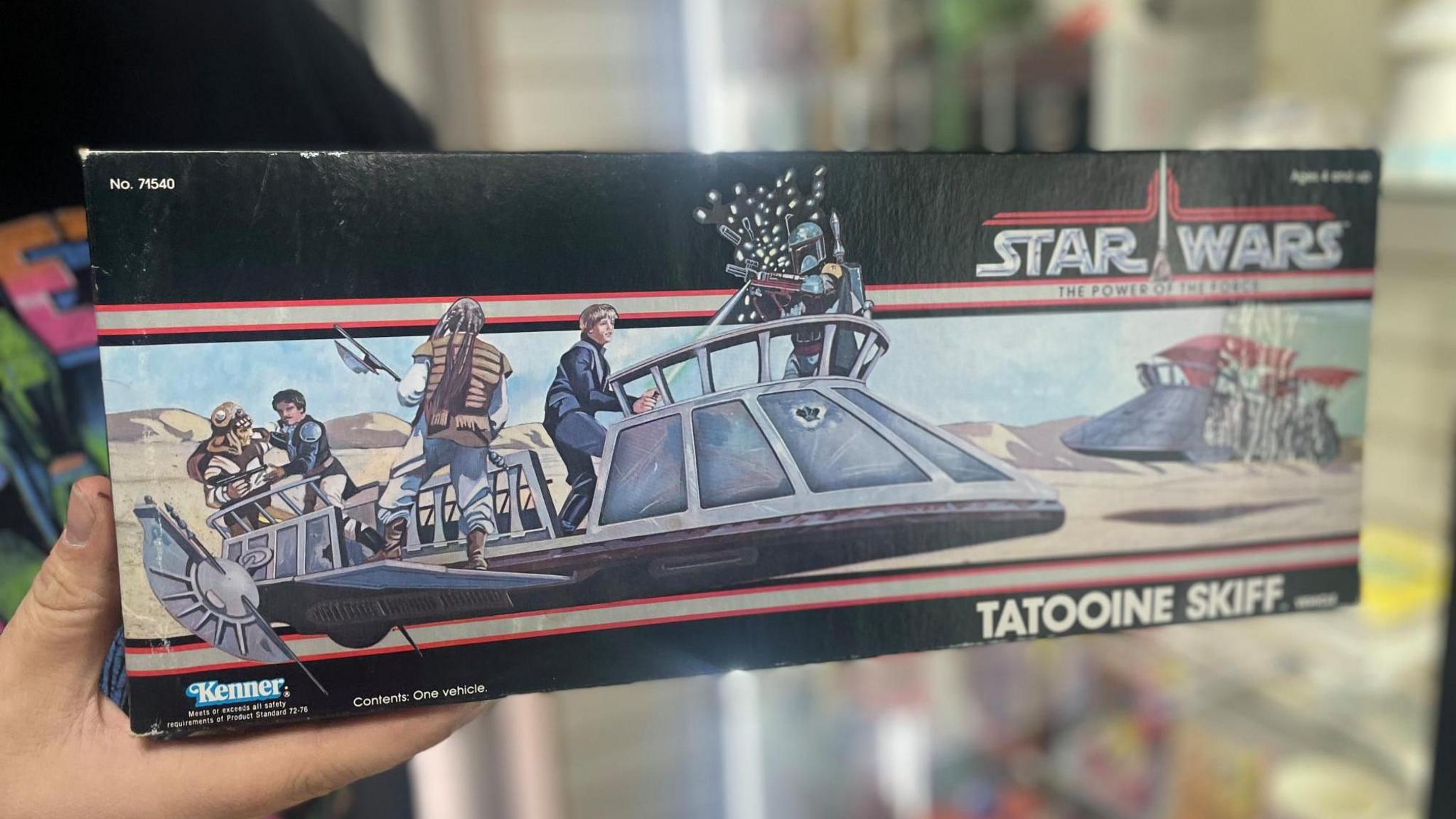 A black box is held up to the camera. The front image shows an aircraft containing several characters hovering above sand.