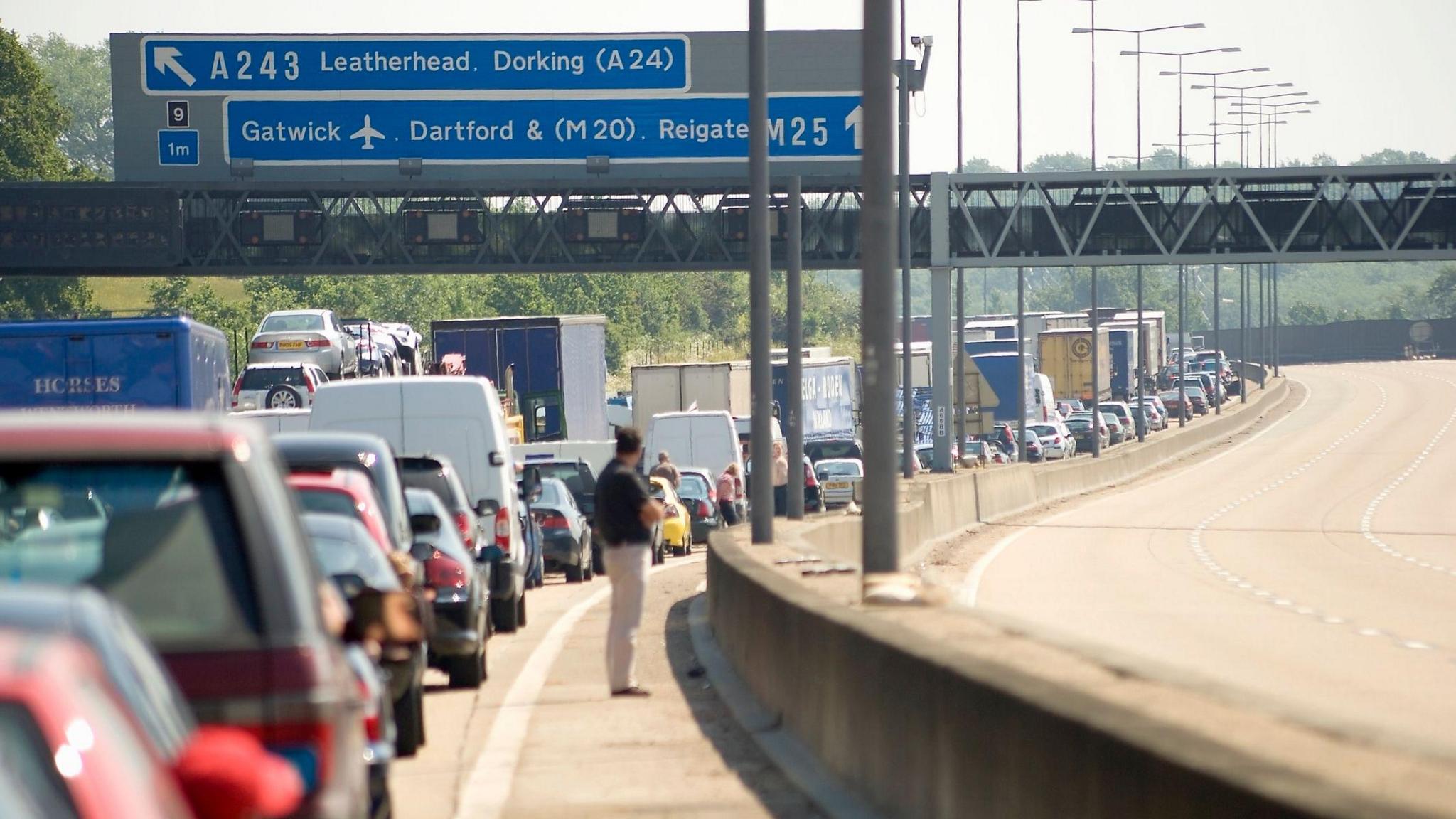 Man stands besides cars queuing on M25