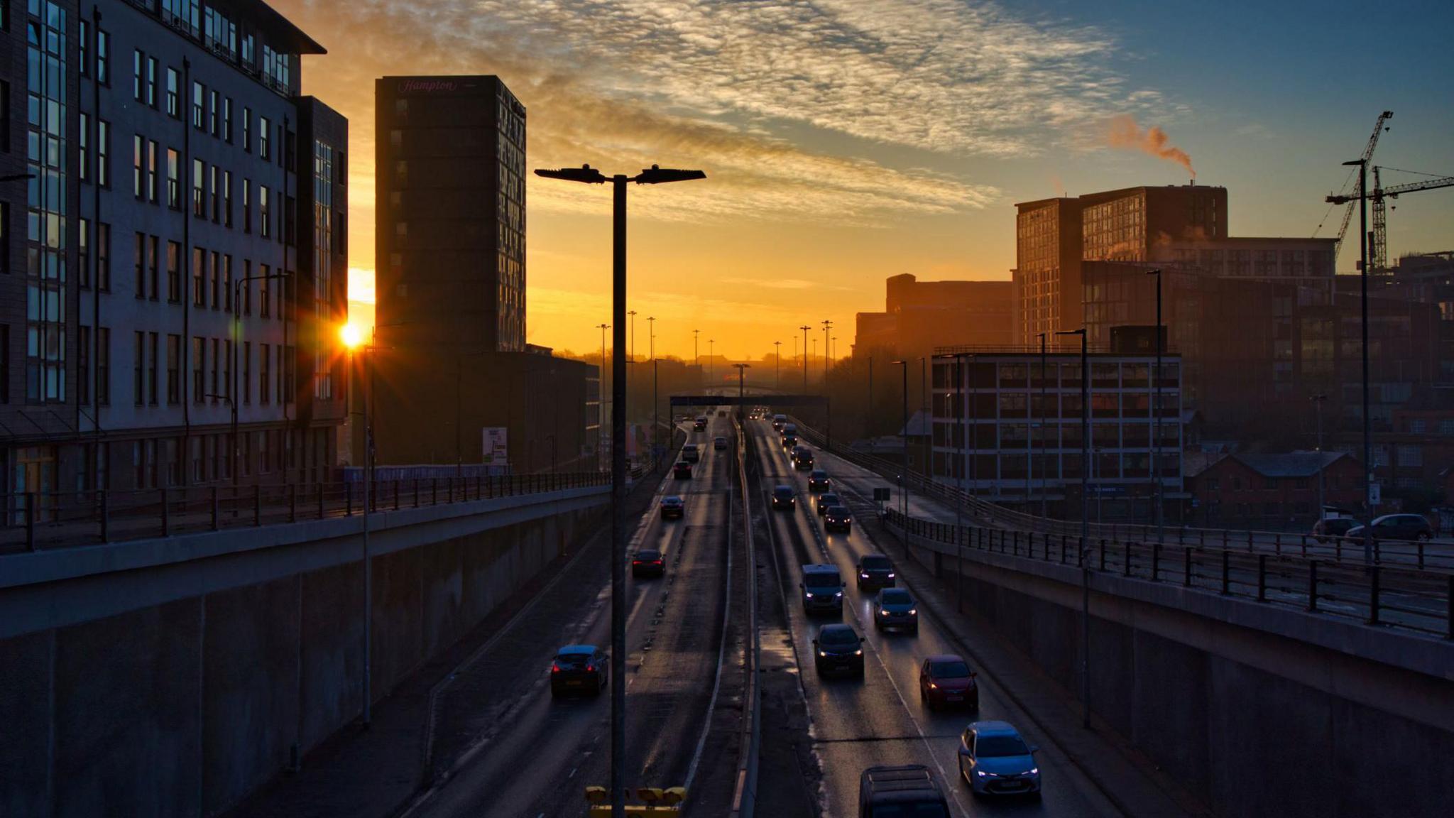 Cars with headlights on at sunset entering and leaving underpass on dual carriageway in Leeds city centre