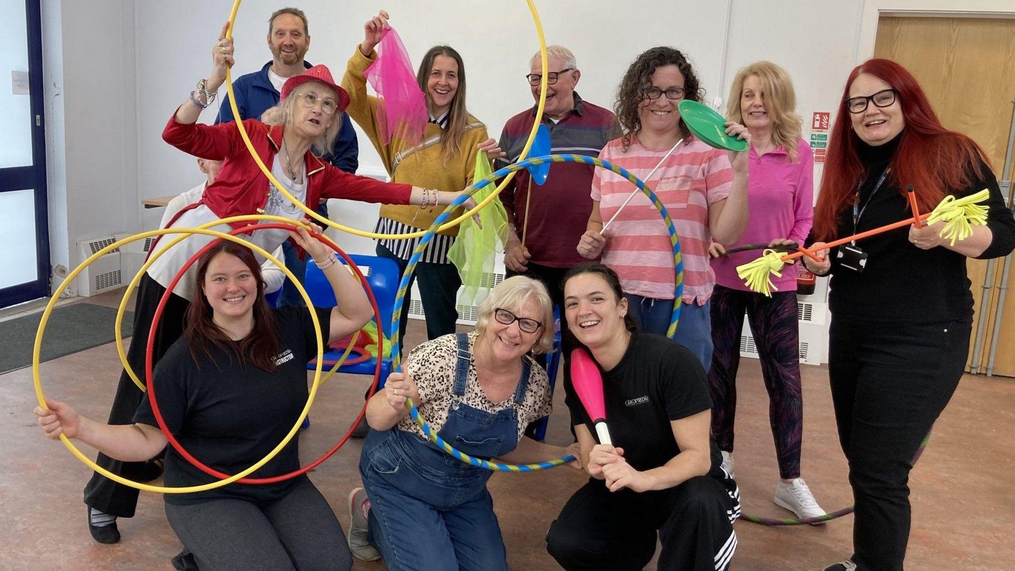 A group of people stand posing for the camera with circus equipment including brightly coloured hoops and plastic plates at the Knowle West Health Centre