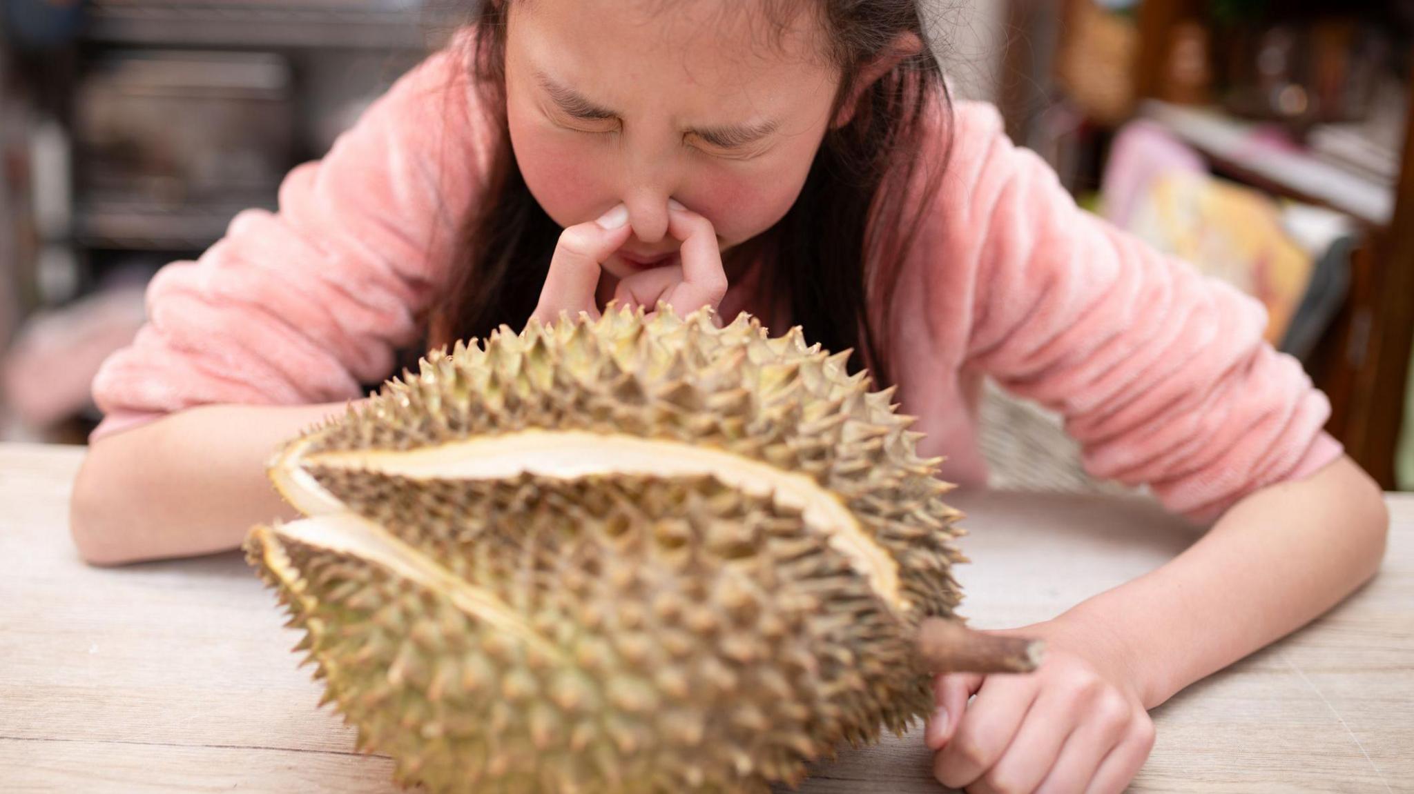 Girl holding her nose in front of Durian fruit. 