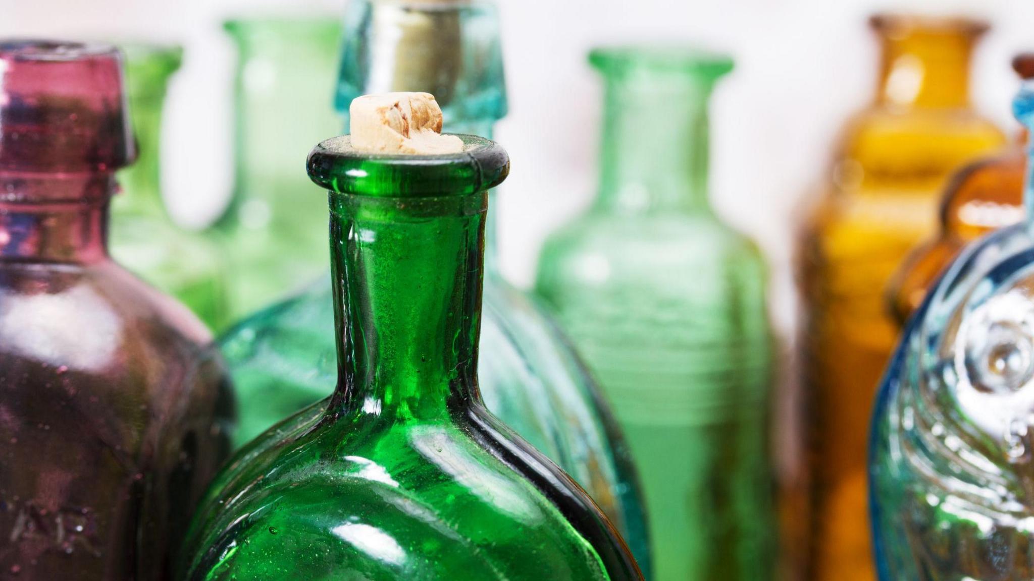 A selection of purple, green, blue and amber glass bottles on a white background. Just the upper section of the bottles can be seen.