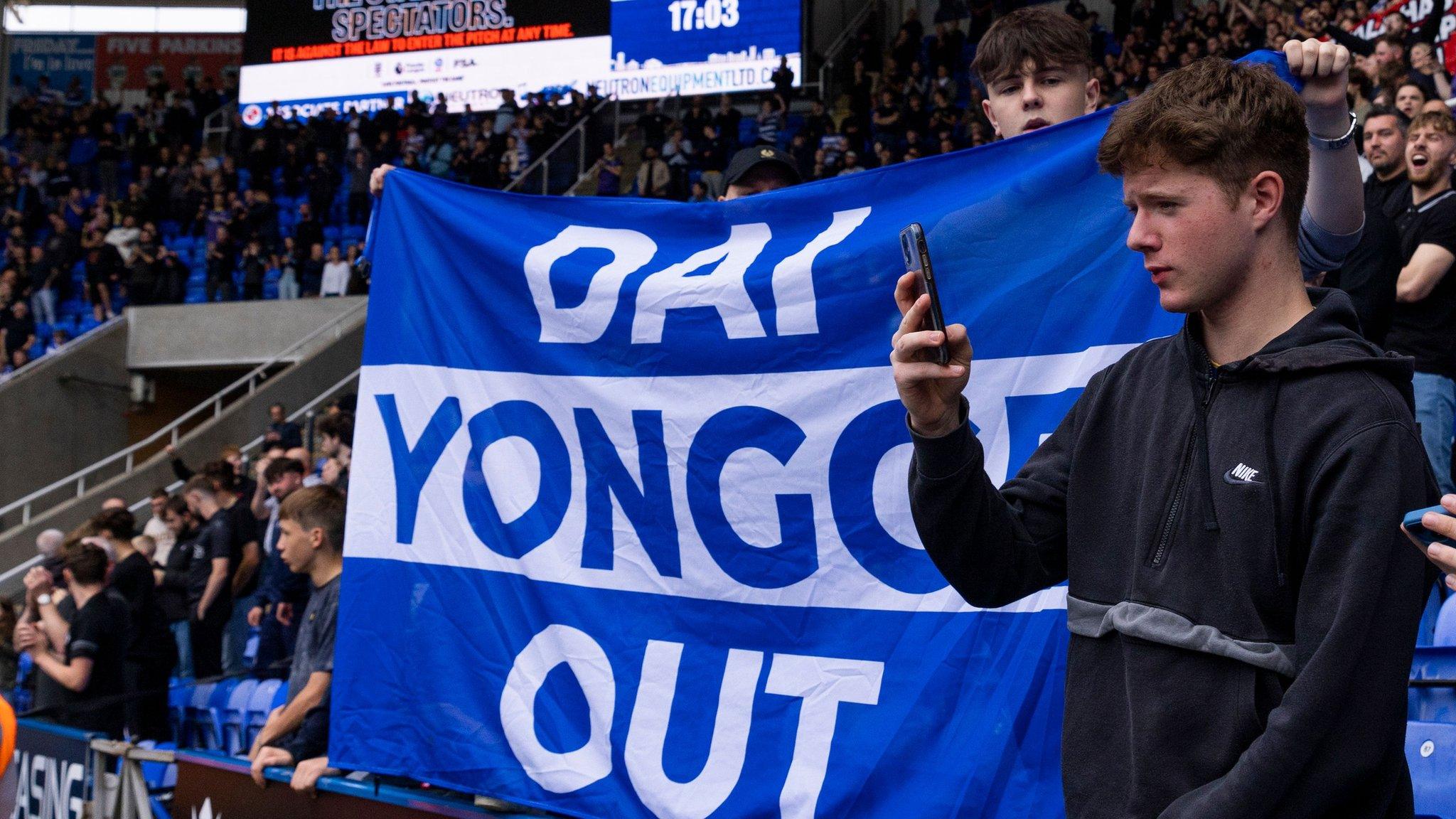 A 'Dai Yongge Out' banner is held up by a Reading fan