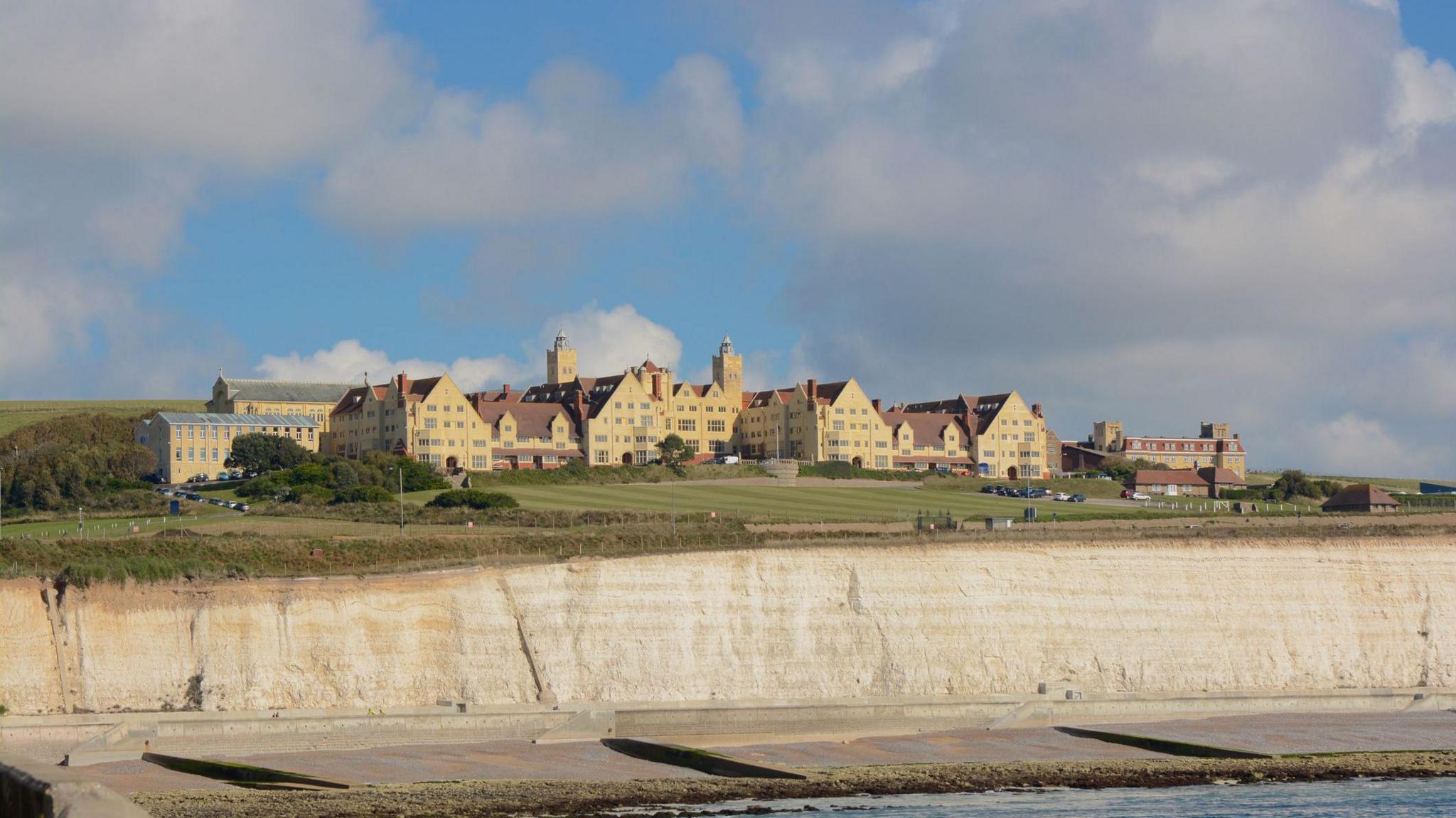 A large yellow complex of 19th-century buildings sits on a white cliff top.