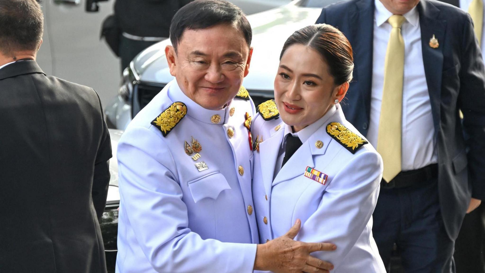 Thaksin and his daughter Paetongtarn embrace each other while wearing white military-like regalia